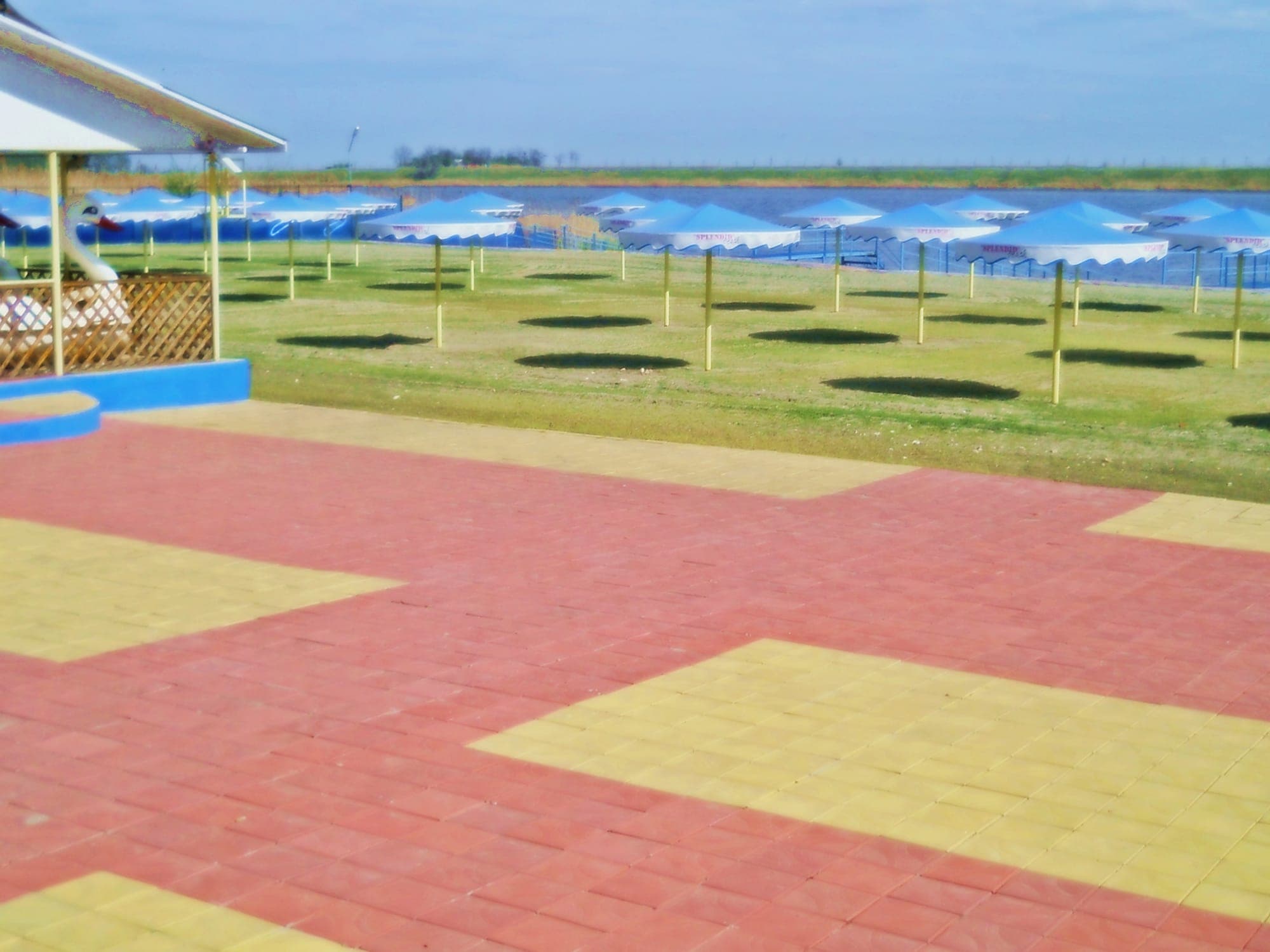 Der Strand Splendid des Hotels Ialomița, mit Reihen blauer Sonnenschirme auf dem Rasen und dem See dahinter