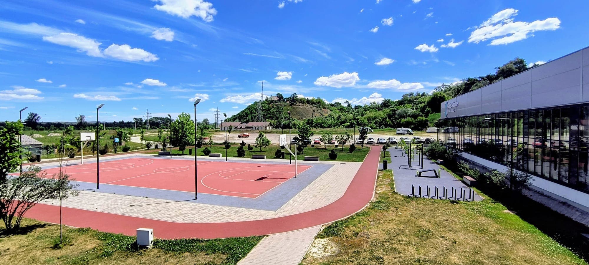 The basketball court and running track in front of the complex, with the car park and the wooded hill in the background