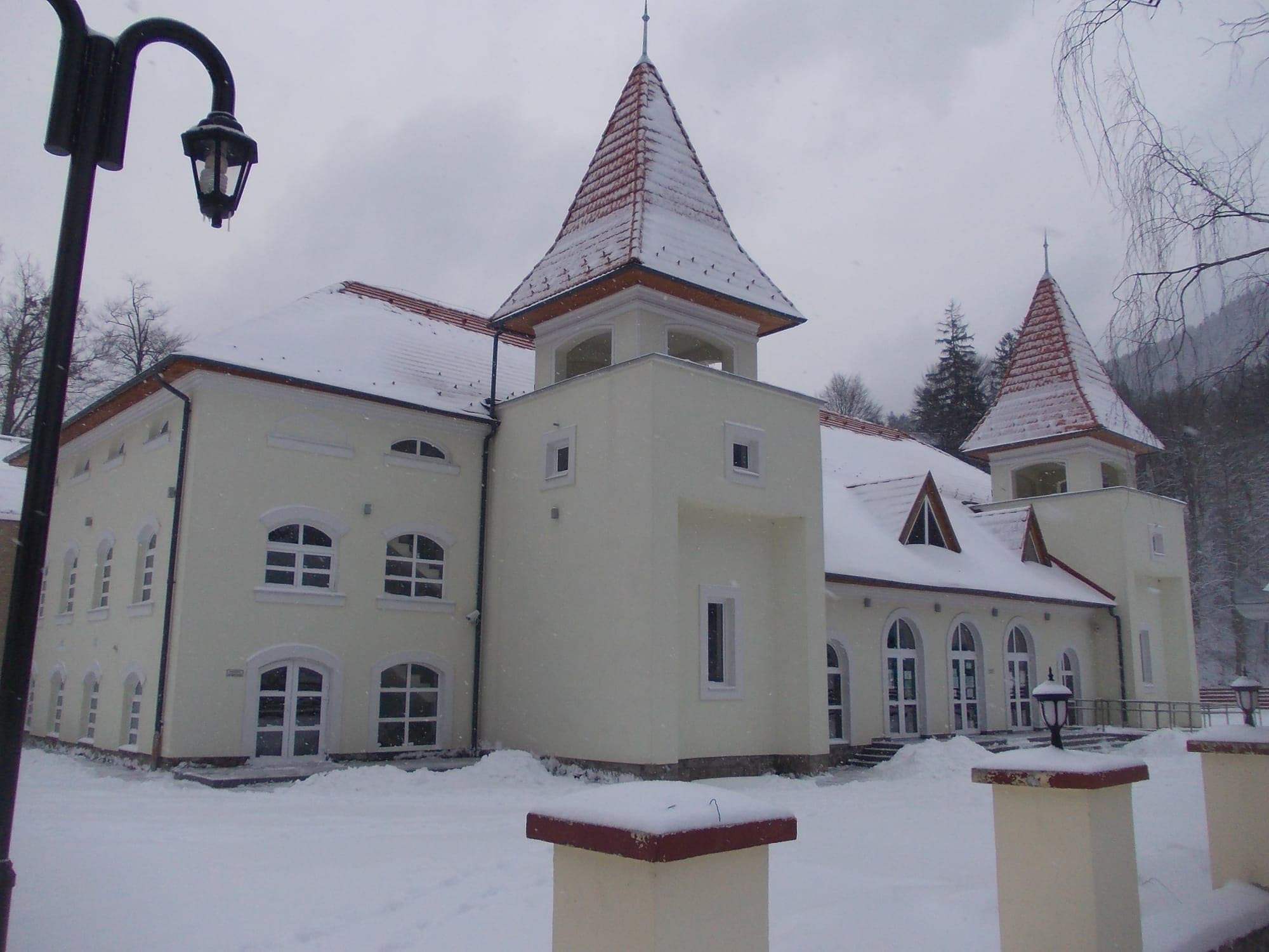 Clădirea albă a centrului spa din stațiune, cu două turnuri cu acoperiș ascuțit, după o ninsoare