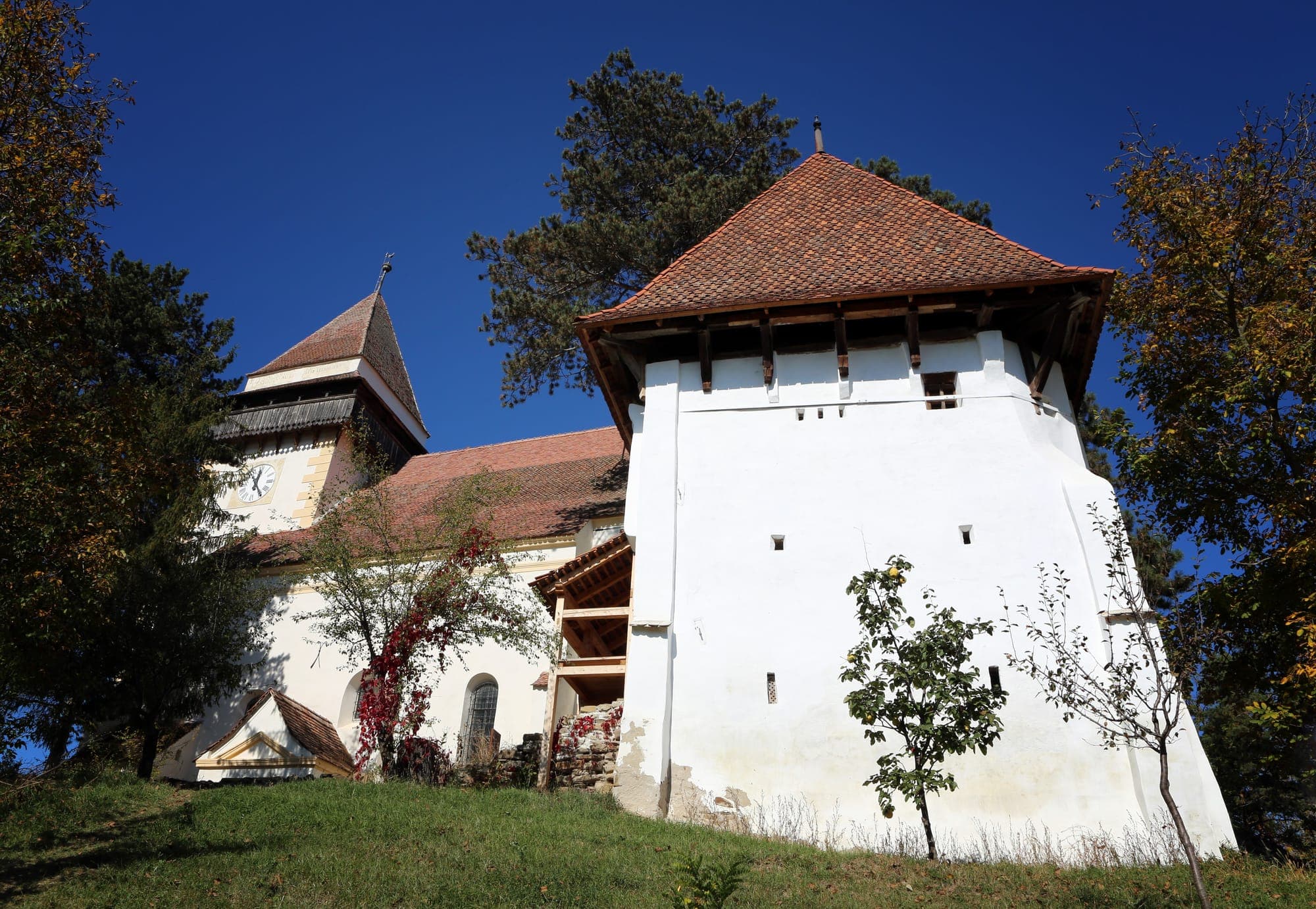 Der weiße Wehrturm mit spitzem Ziegeldach und links der Glockenturm mit Uhr, vom Hügel von unten gesehen, unter blauem Himmel