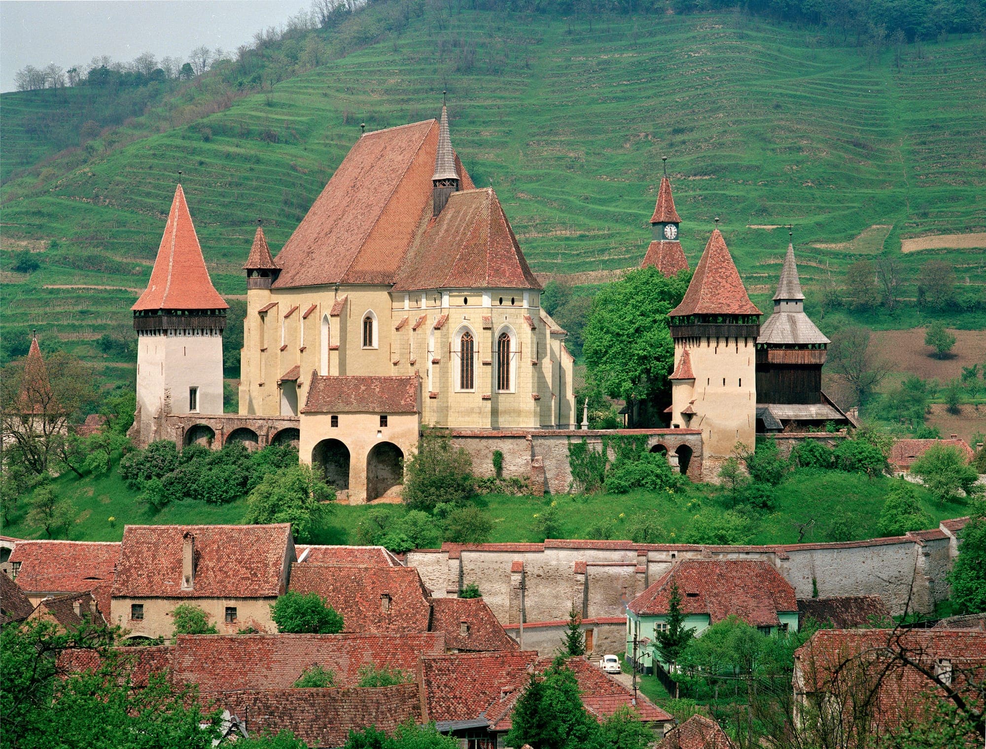 Biserica fortificată cu turnurile și zidurile ei, deasupra acoperișurilor satului, cu dealul cu vii terasate în spate