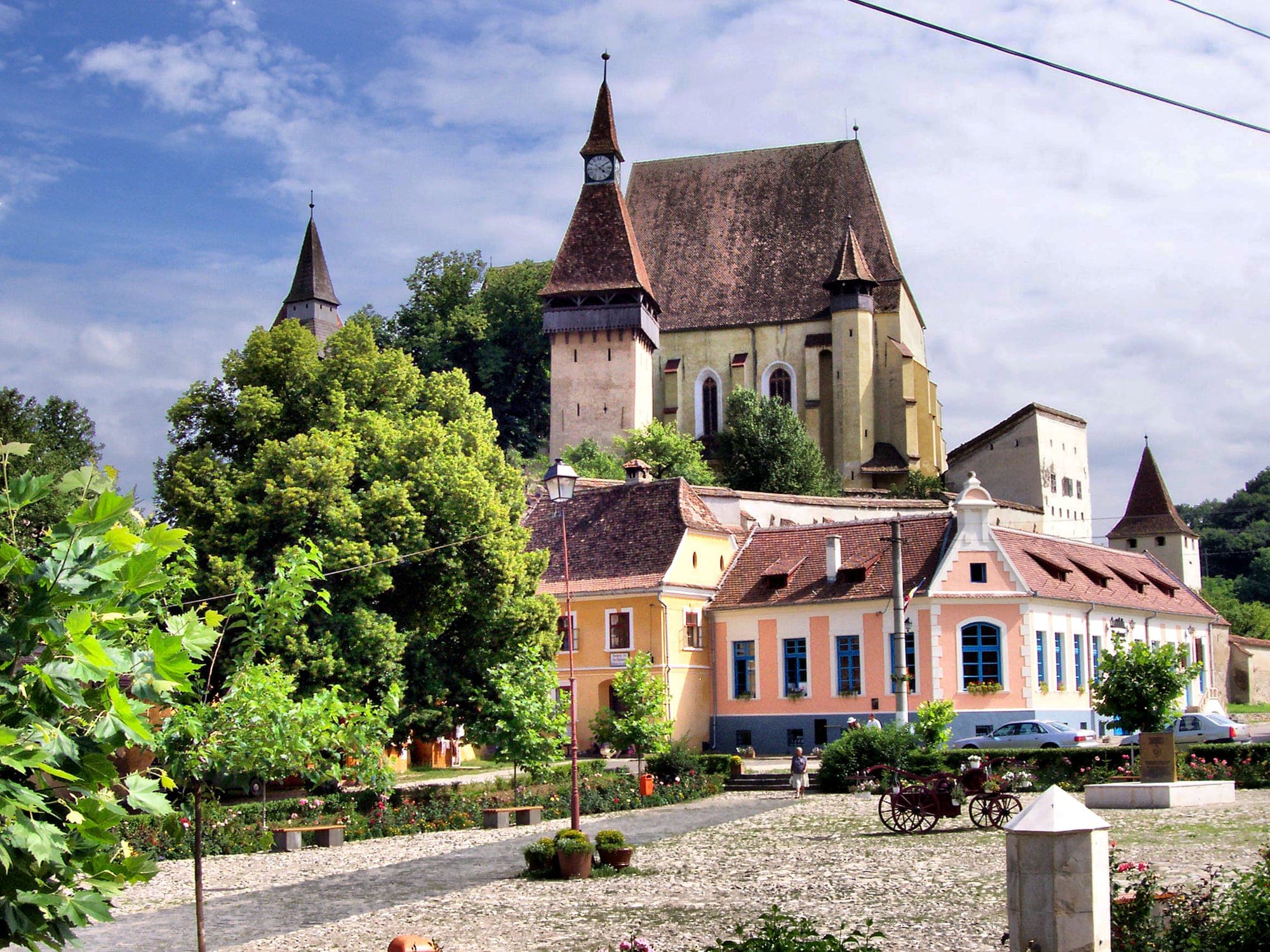 Piața satului cu casele colorate din față, iar deasupra lor turnul cu ceas și biserica