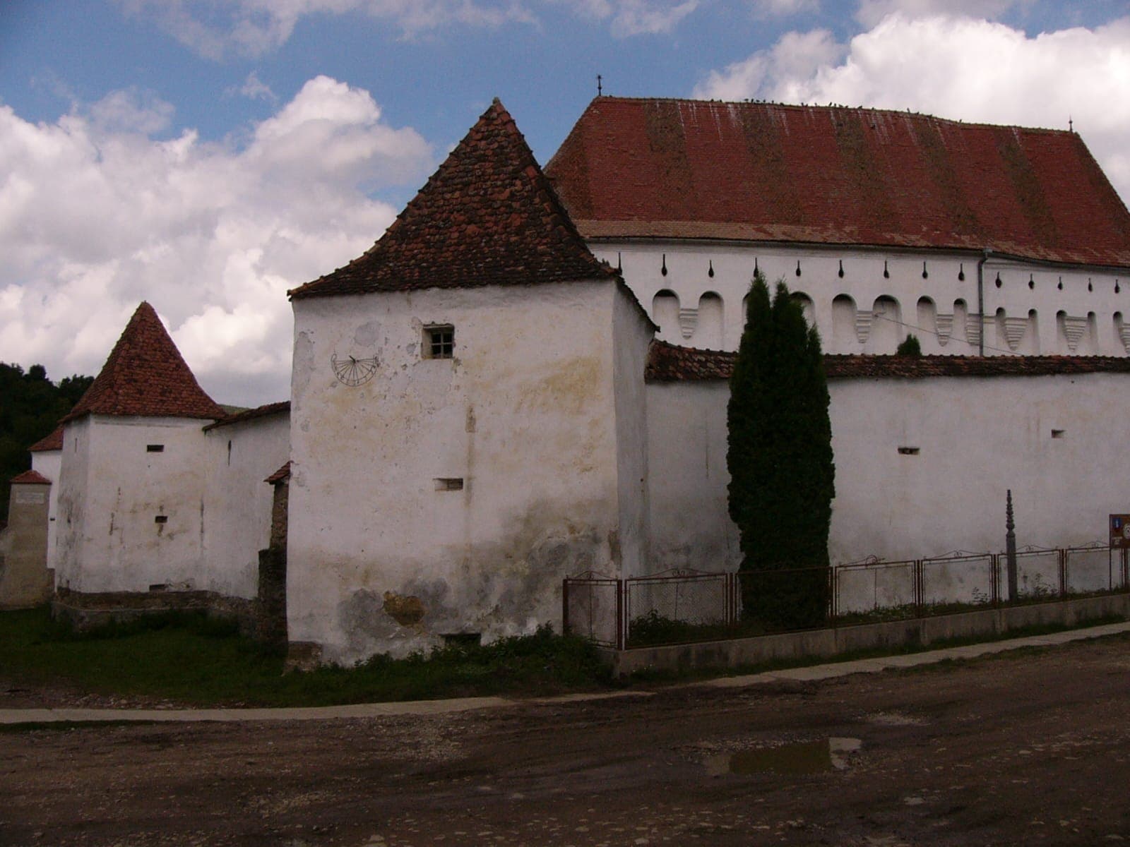 Zidul alb al cetății cu un bastion de colț cu acoperiș în pantă, deasupra căruia se ridică biserica cu etajul de apărare și acoperișul înalt de țiglă