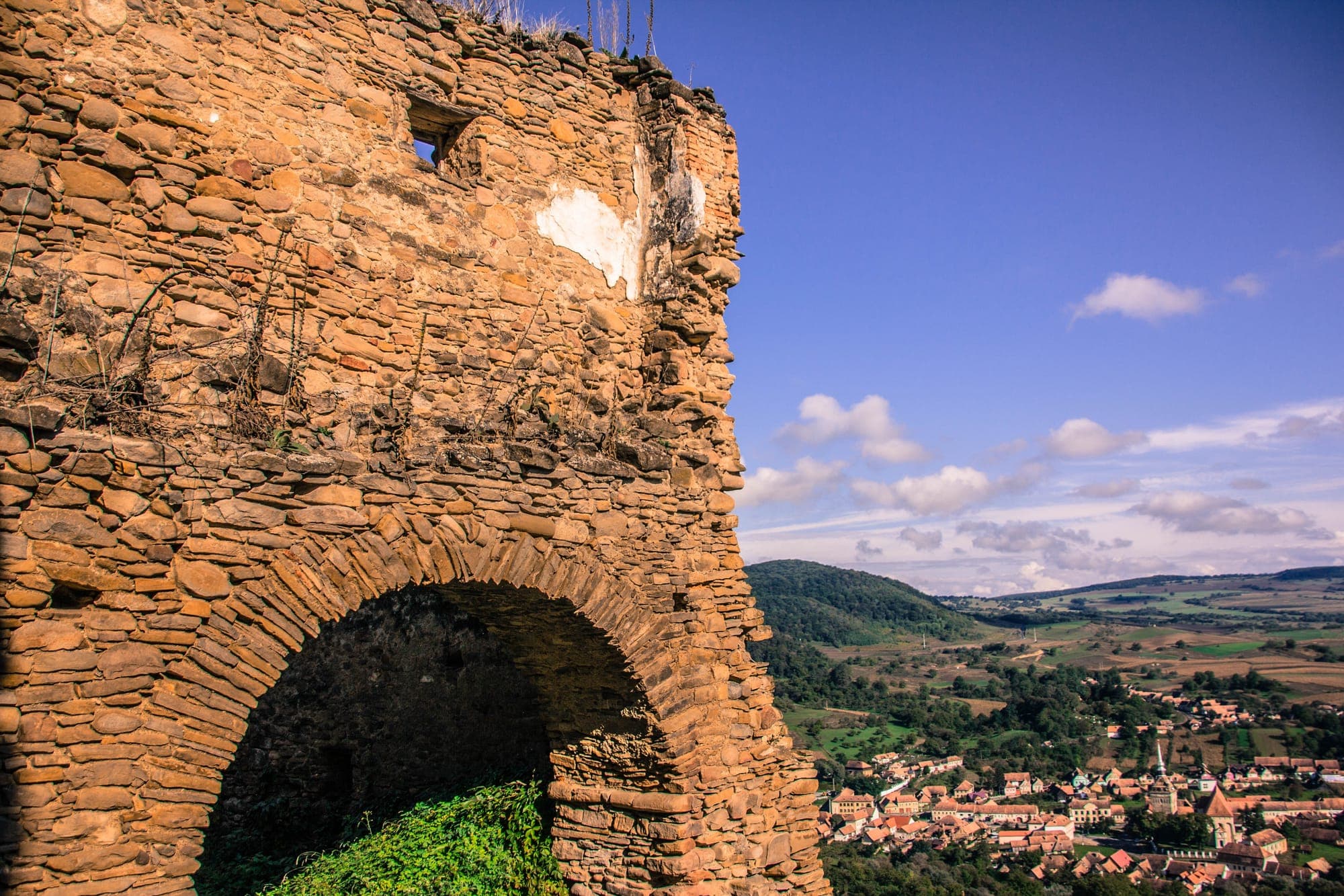 A stone tower of the peasant fortress with an arch, and the village of Saschiz with the church tower in the valley below