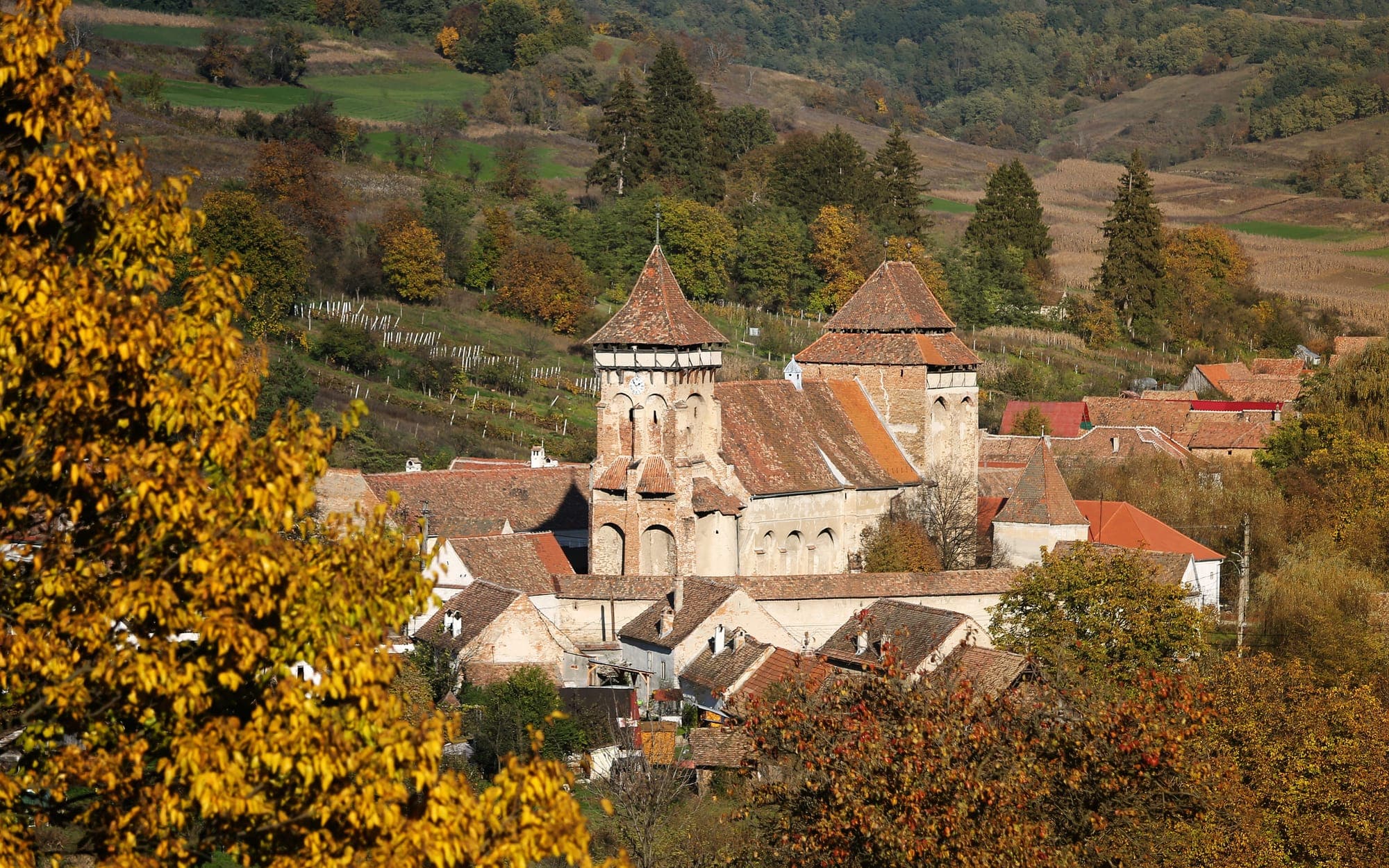 Biserica fortificată cu turnul-clopotniță și corul fortificat, între acoperișurile satului, cu dealuri și vii toamna