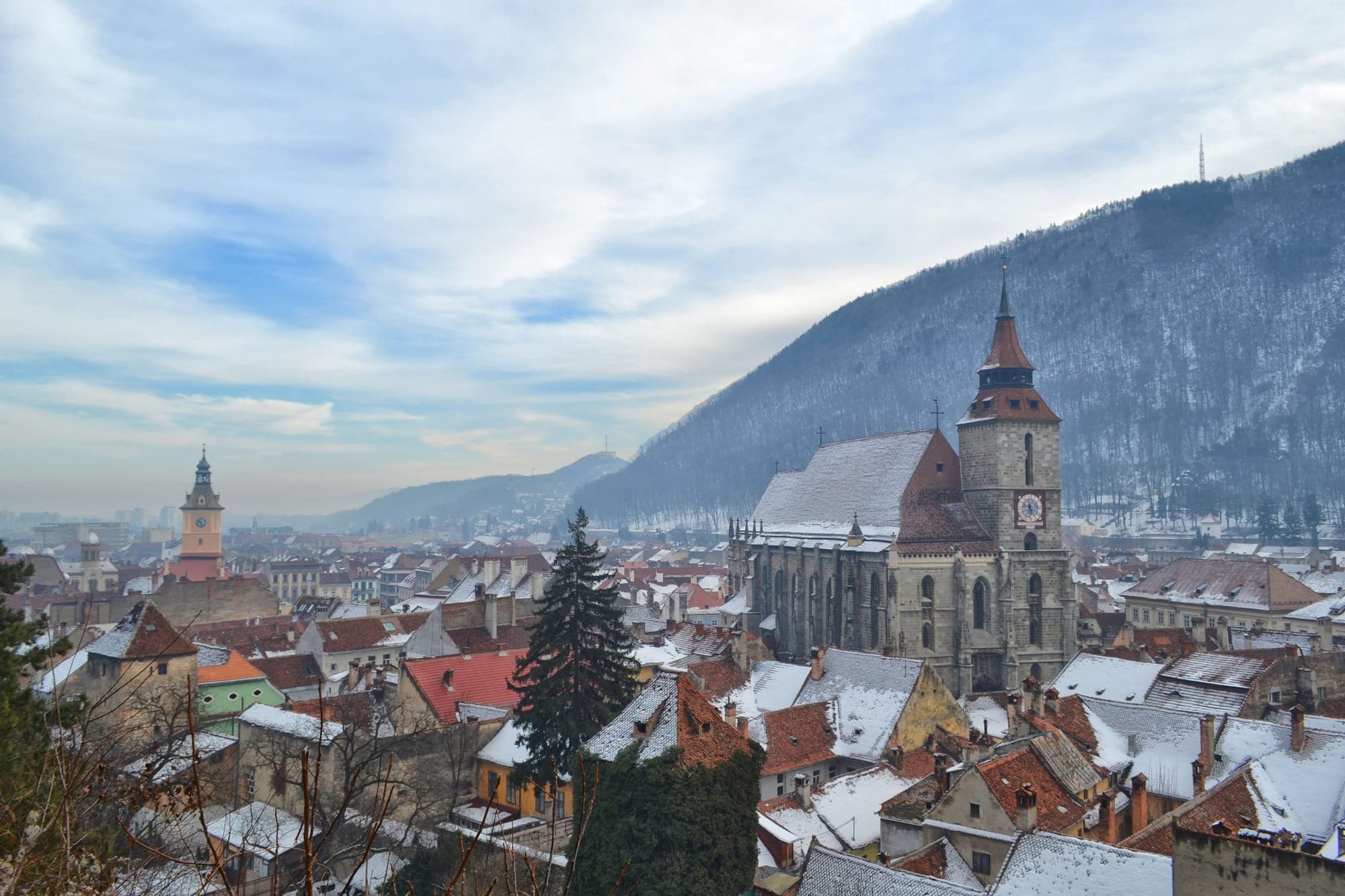 Biserica Neagră cu turnul cu ceas deasupra acoperișurilor înzăpezite ale centrului vechi, cu Tâmpa în dreapta și turnul Casei Sfatului în stânga