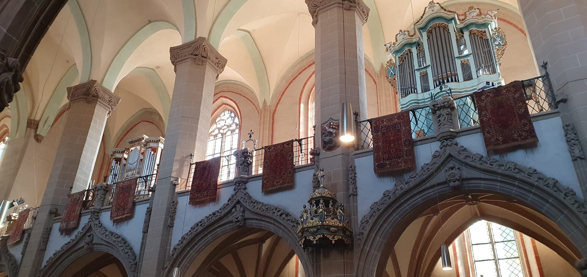 Die Emporen im Inneren mit roten orientalischen Teppichen an den Brüstungen, Steinpfeilern, Gewölben und einer Orgel auf der Empore