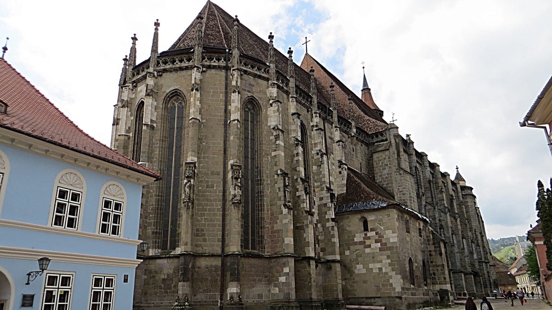 Der gotische Chor der Kirche mit hohen Fenstern und Strebepfeilern mit Figuren, von der gepflasterten Gasse zwischen alten Häusern aus gesehen
