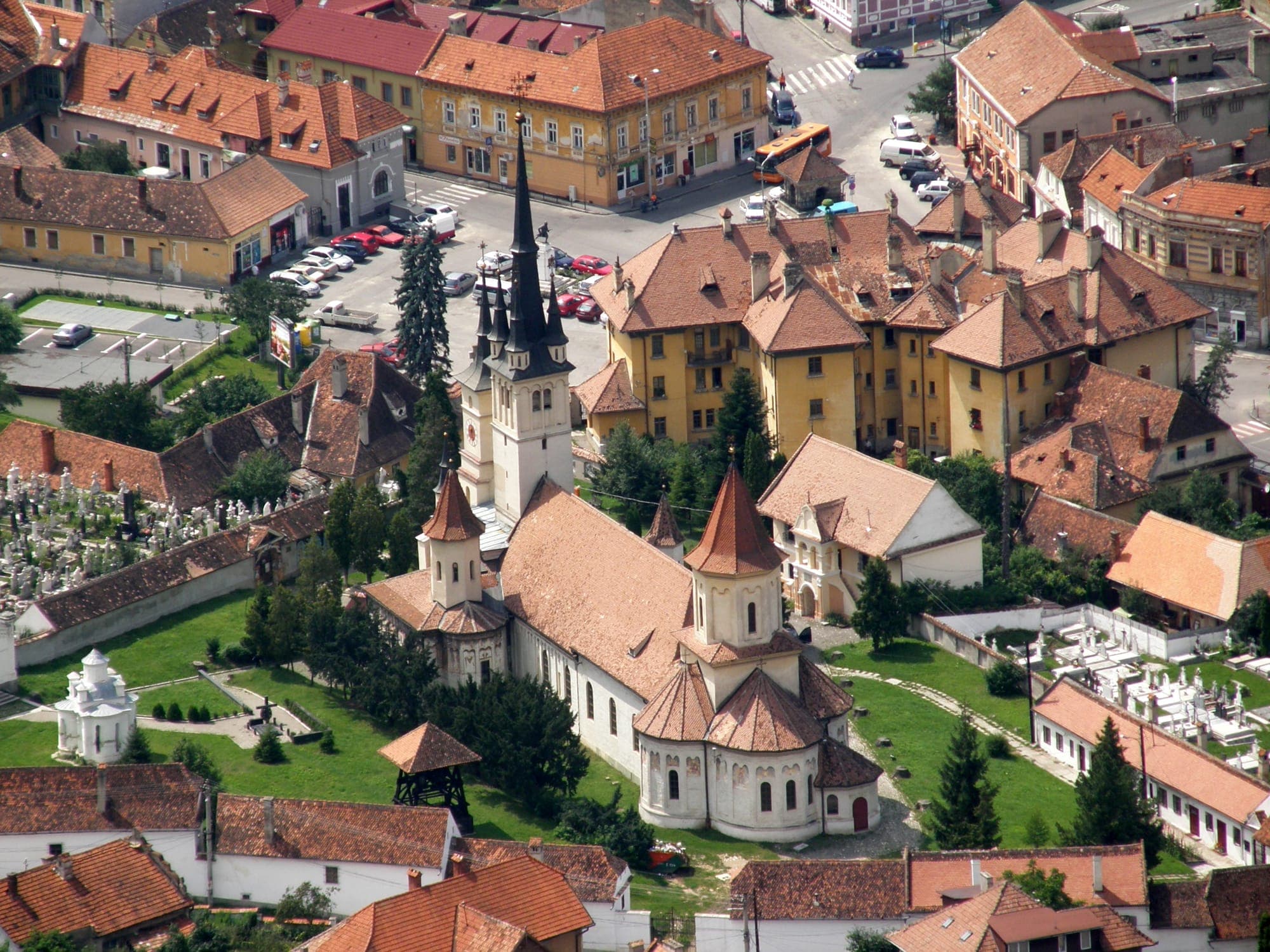 Die Kirche von oben mit ihren Türmen, dem grünen Hof, dem weißen Weihwasserbrunnen und dem Friedhof dahinter, zwischen den Häusern von Șchei
