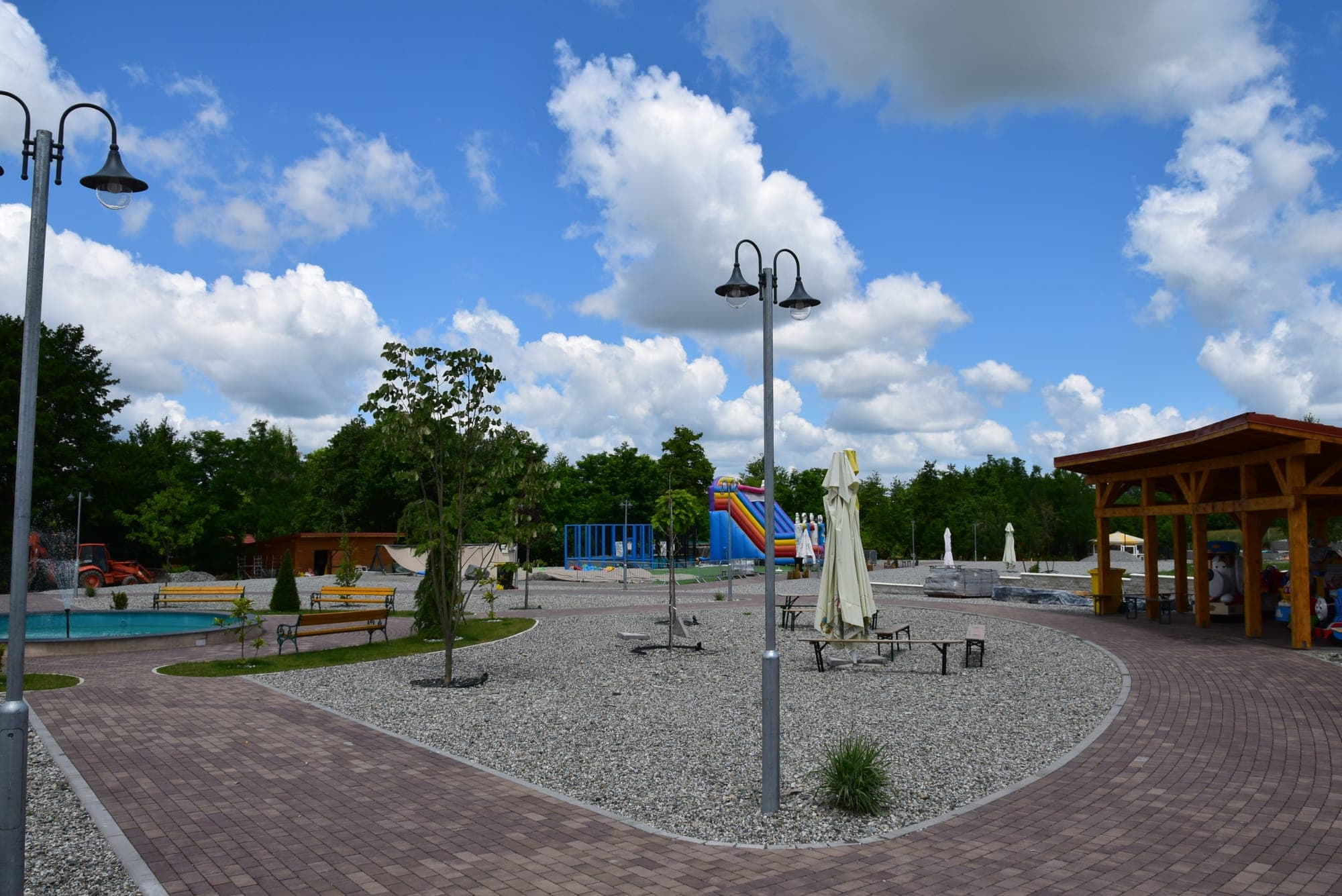 Der gepflasterte Platz im Park mit Bänken, einer Holzpergola und bunten Rutschen im Hintergrund