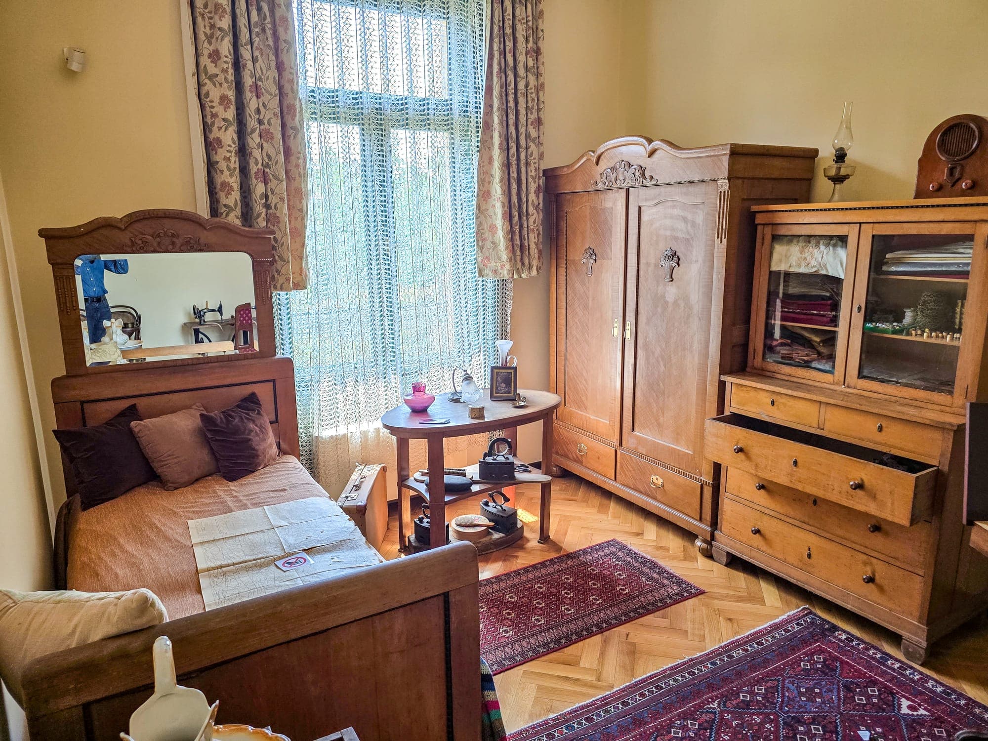 Una camera ricostruita con letto, specchio, armadio e vetrina in legno d'epoca, su un parquet con tappeti