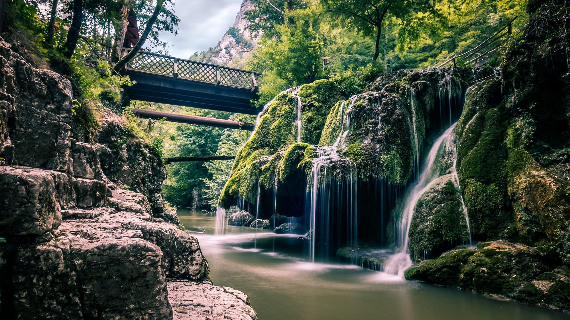 Cascada Bigăr înainte de prăbușirea din 2021: ciuperca de tuf acoperită de mușchi, cu voalul de apă căzând în Miniș, sub puntea de lemn