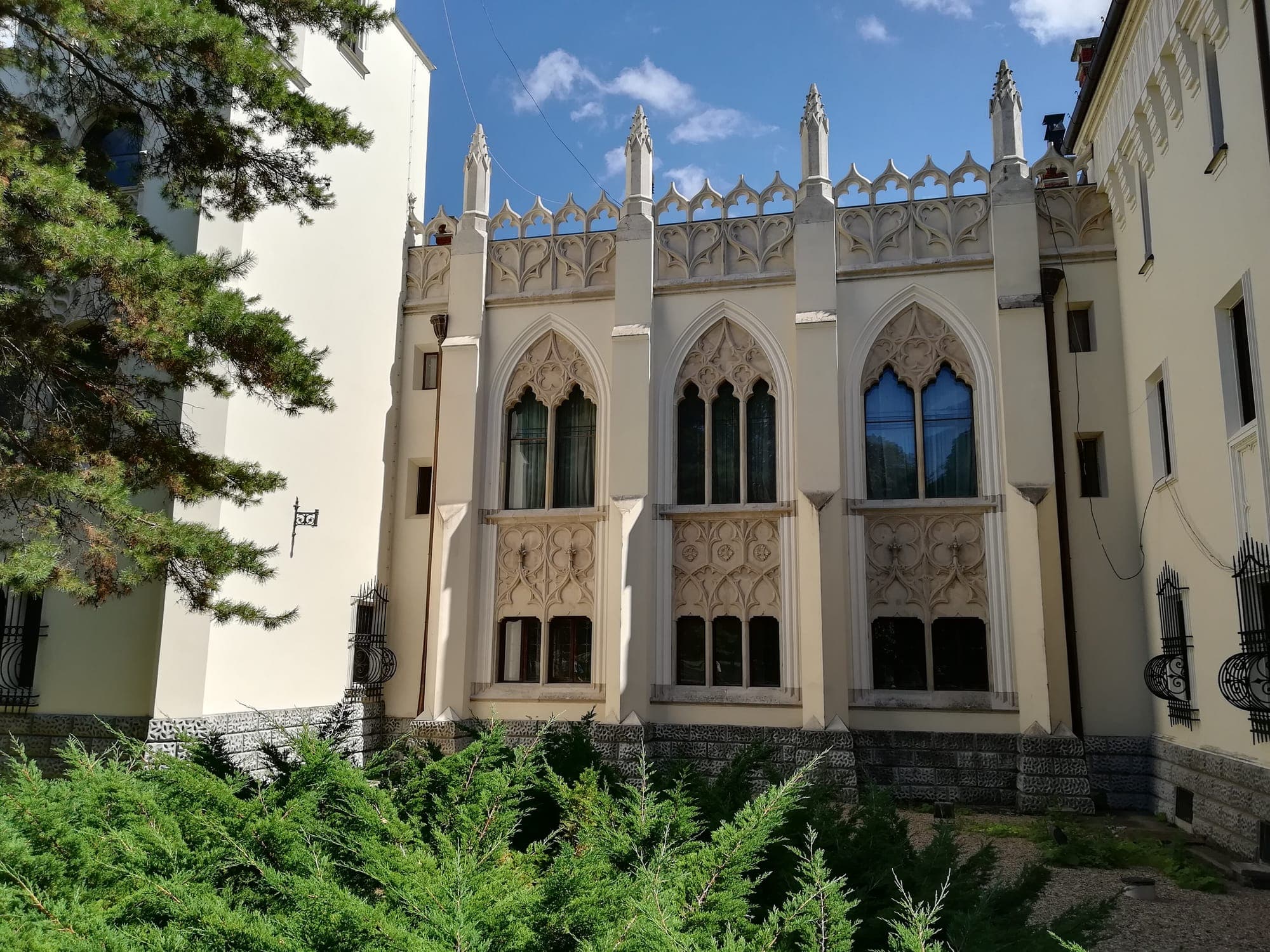 Fațada capelei castelului, cu ferestre gotice, fleuroni și balustradă traforată, văzută din parc