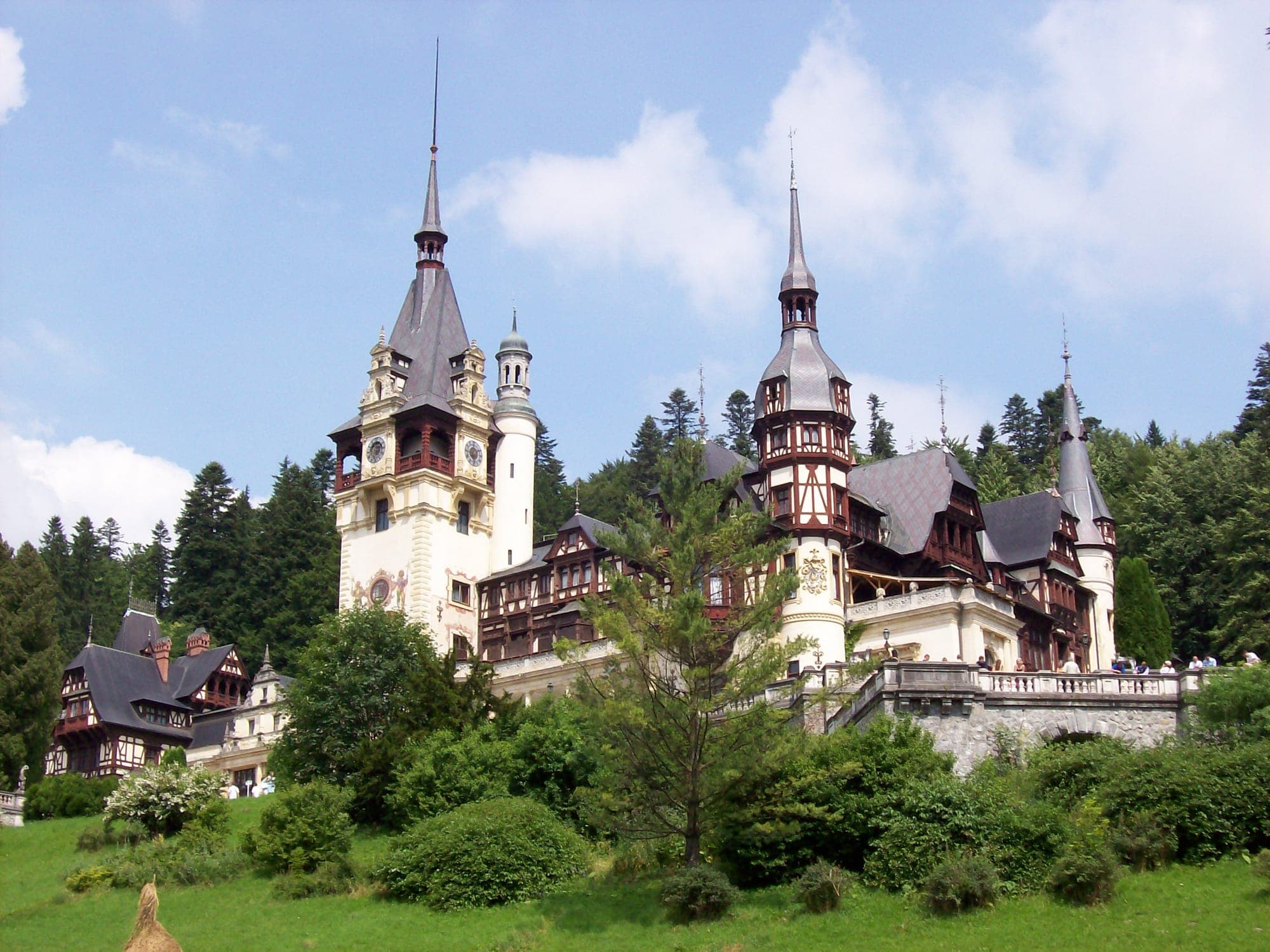 Castelul, cu turnul cu ceas și turnurile ascuțite cu fachwerk, văzut de pe pajiștea de sub terase, într-o zi de vară