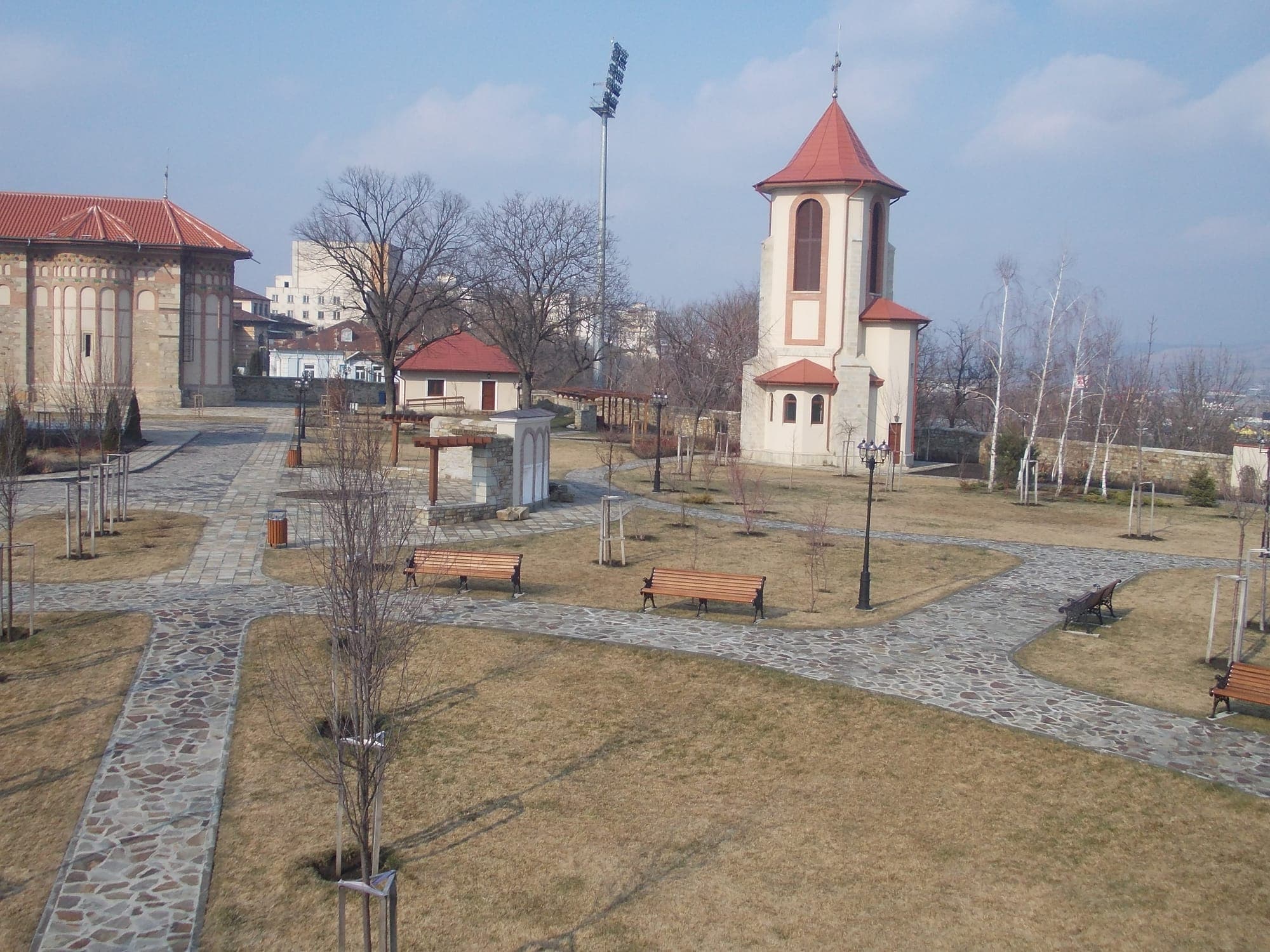 Der Archäologiepark von oben, mit gepflasterten Wegen, Bänken, dem neuen Glockenturm und der Kirche links