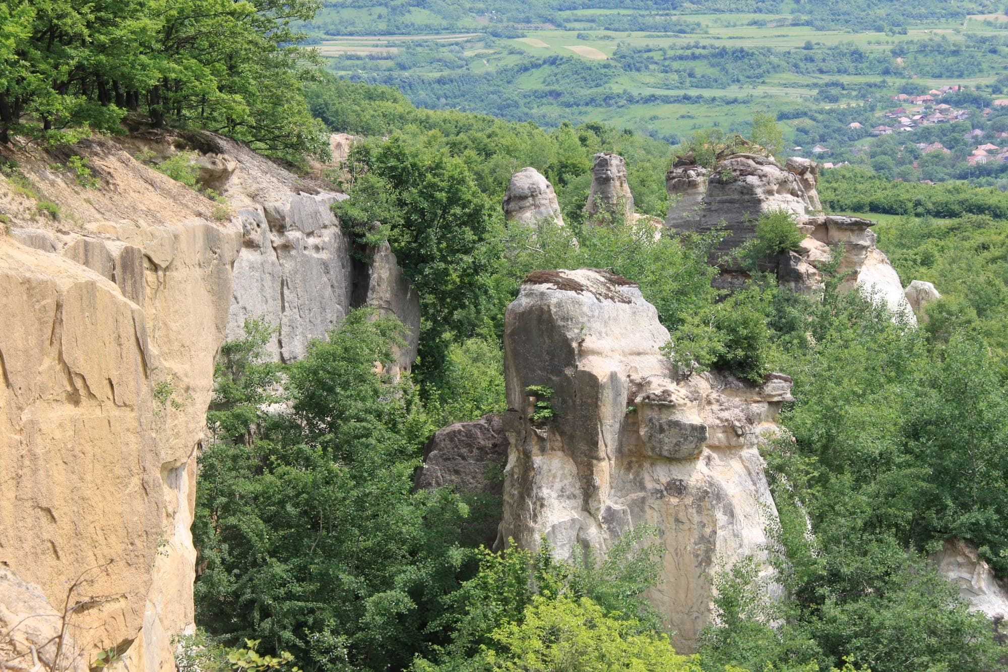 Sandsteinsporne und -türme, die aus den Bäumen ragen, mit dem Dorf in der Ferne