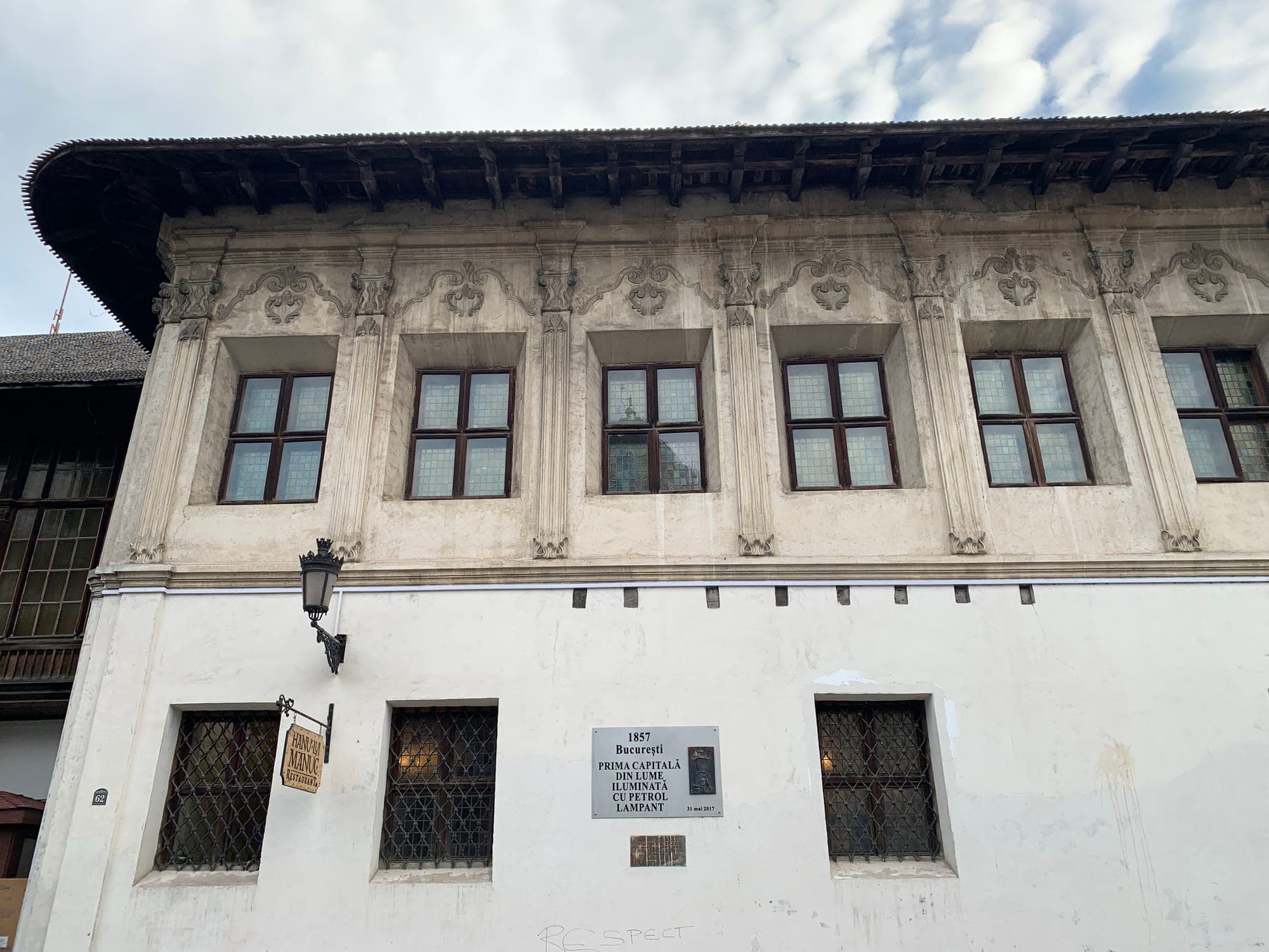 The upper floor of the façade with framed windows and relief ornaments, a wide wooden eave and the plaque about the 1857 kerosene lighting