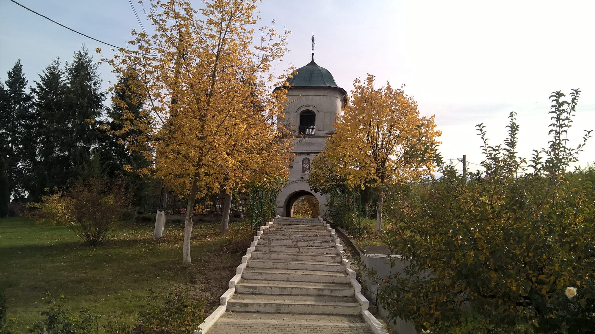 Der Torglockenturm mit grünem Dach, vom Ende einer breiten Treppe aus gesehen, zwischen Bäumen mit gelbem Laub