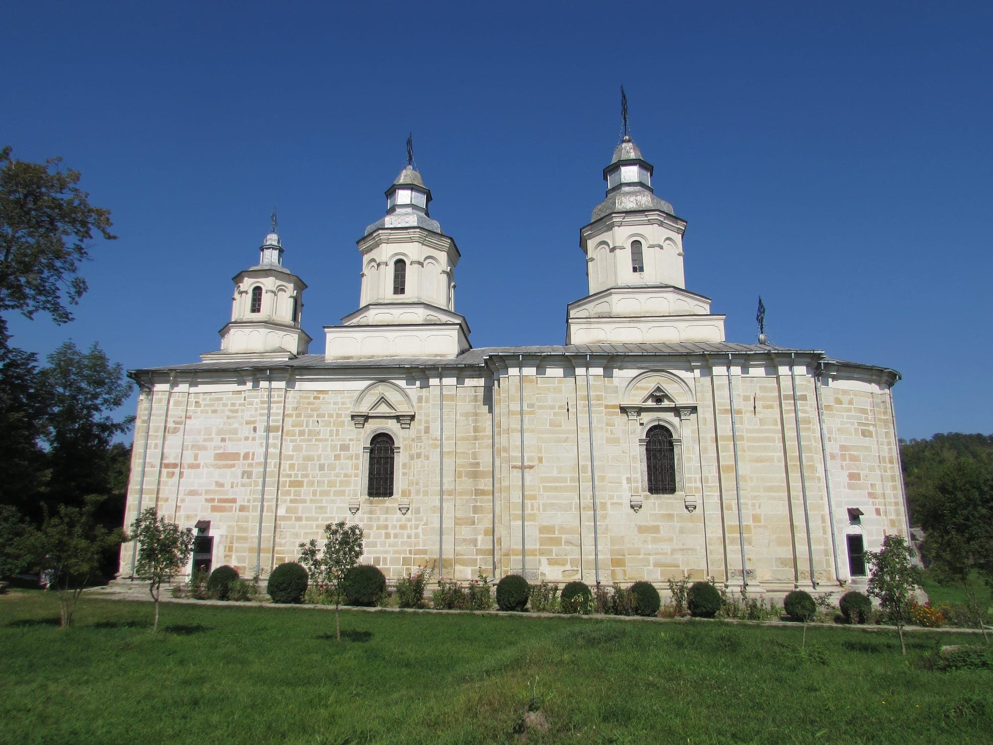 Die Kirche der Heiligen Erzengel von der Seite, mit Fassaden aus behauenem Stein, Fenstern mit gemeißelten Einfassungen und drei weißen Türmen