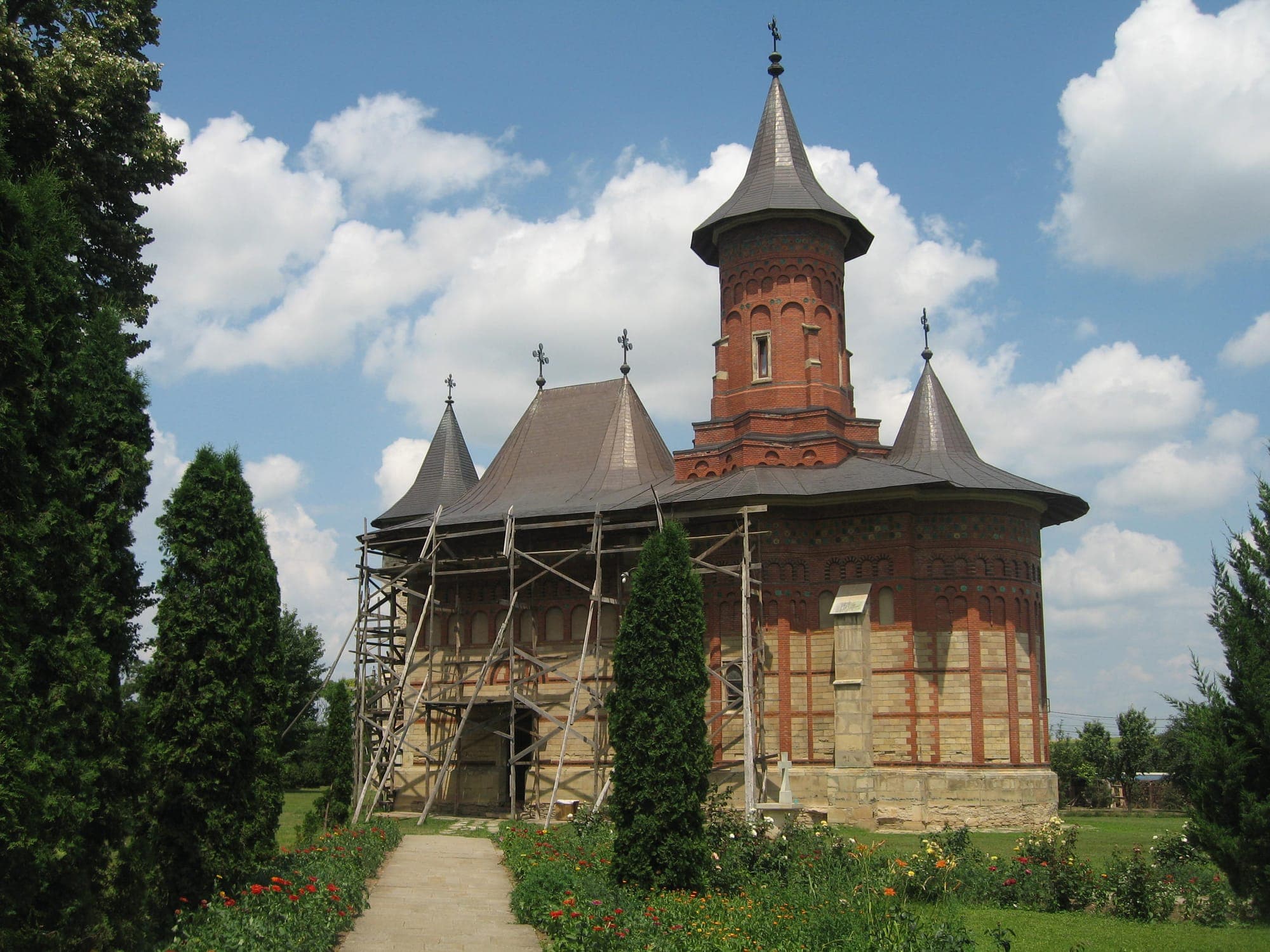 La chiesa di Stefano in mattoni rossi, con l'alta torre sulla navata e il tetto di lamiera, vista da un viale fiorito