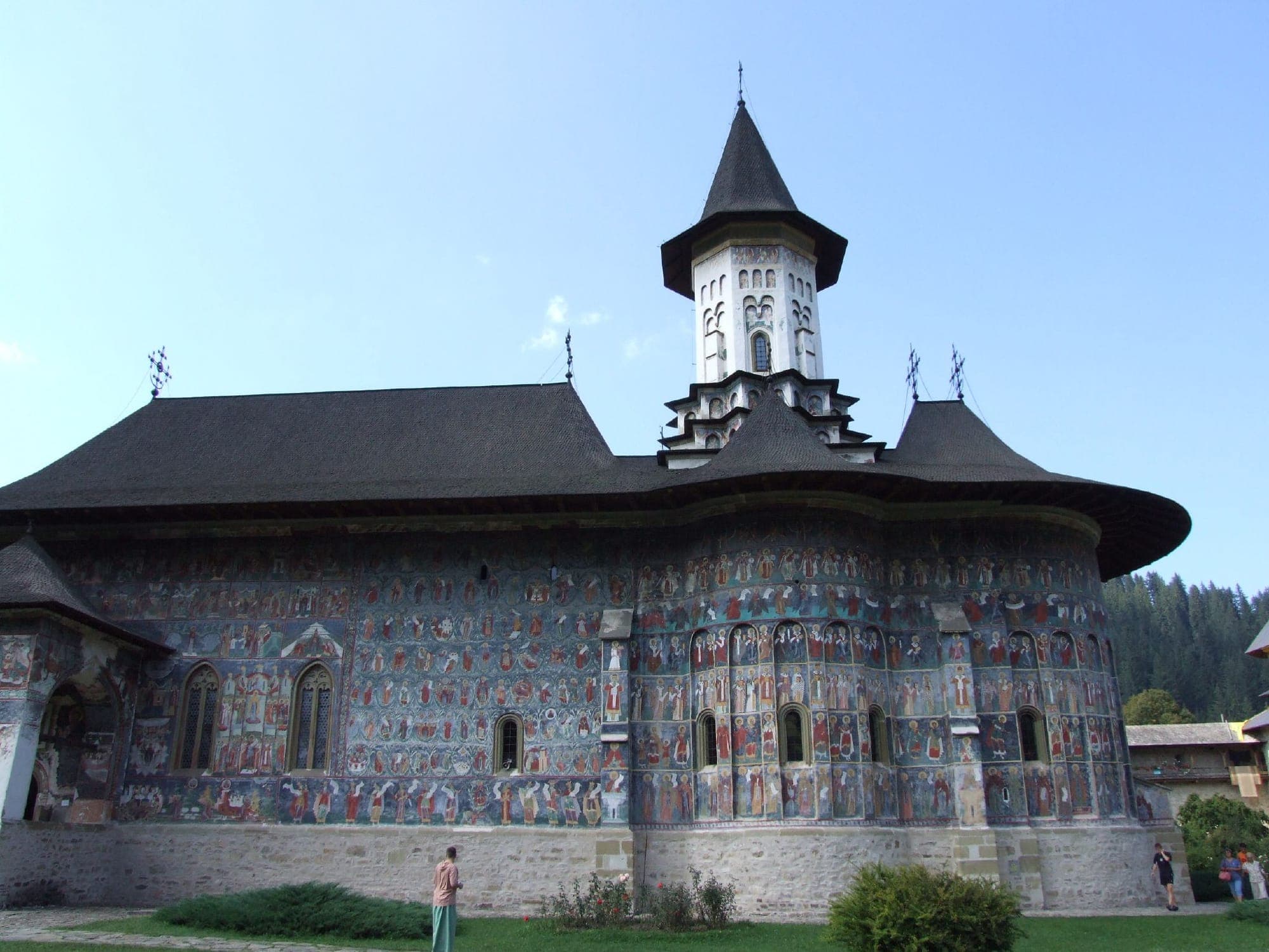 Biserica Învierii văzută dinspre sud-est, cu absidele și fațada de sud acoperite de fresce sub acoperișul larg de șindrilă și turla albă