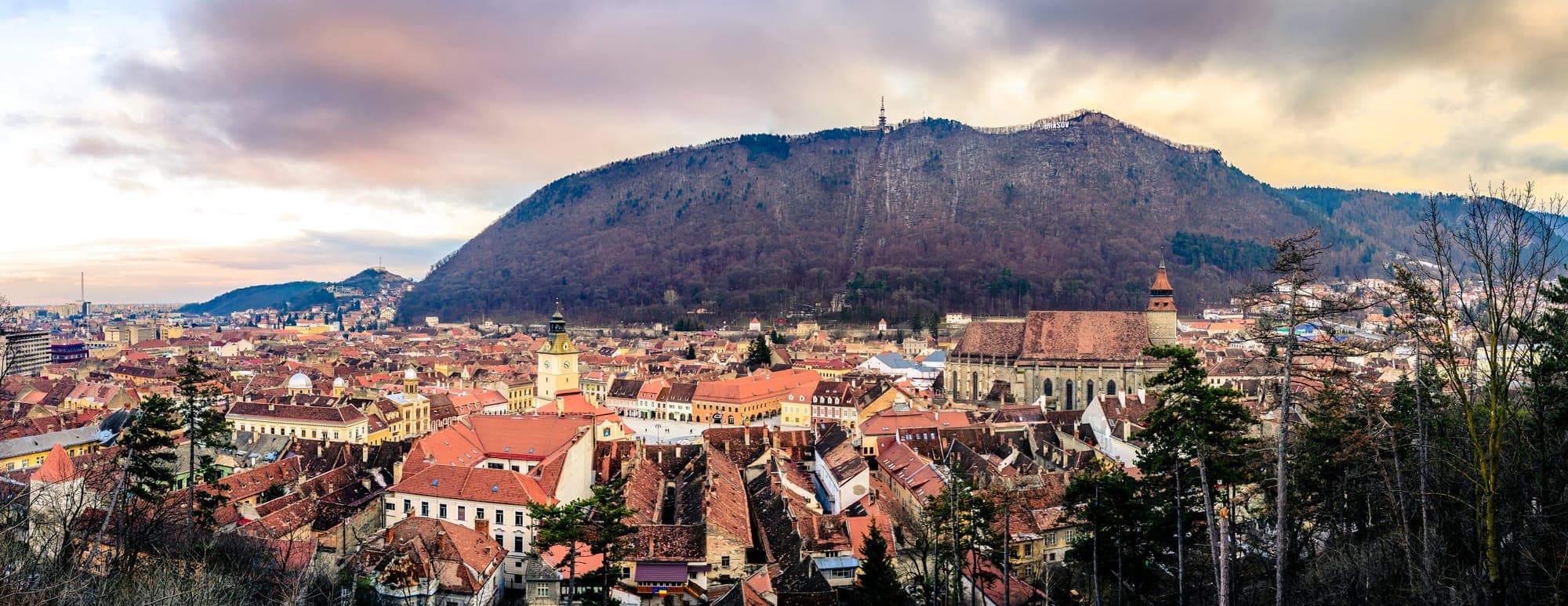 Panorama della città vecchia d'inverno, con la torre della Casa Sfatului e la Chiesa Nera in primo piano e il Tâmpa che si alza alle loro spalle, al tramonto