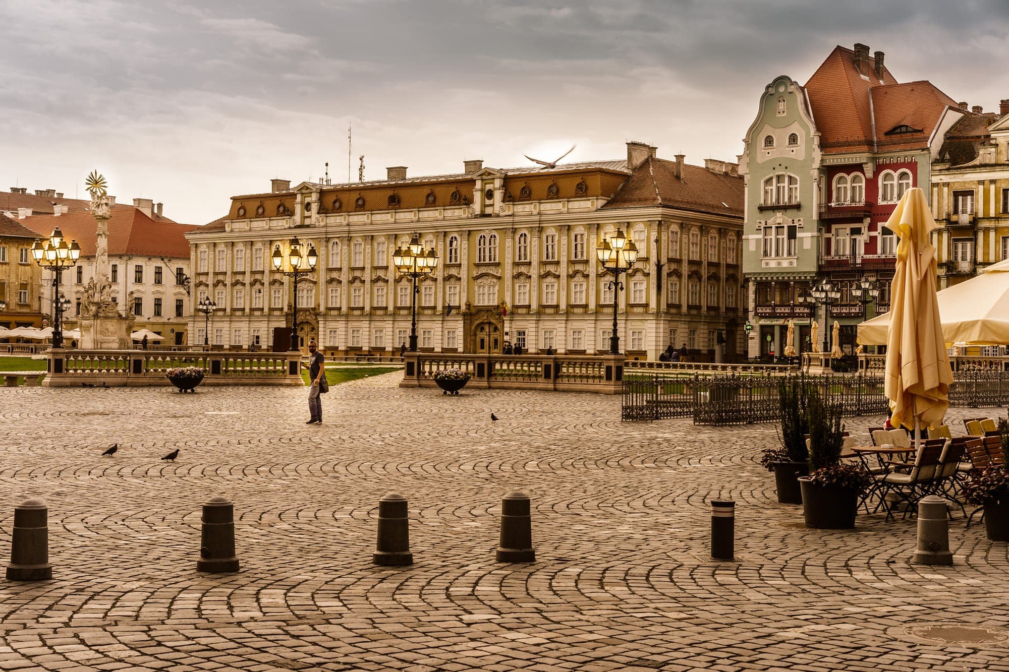 Der Unirii-Platz mit dem Barockpalast im Hintergrund, Straßenlaternen, der Dreifaltigkeitssäule links und bunten Häusern rechts