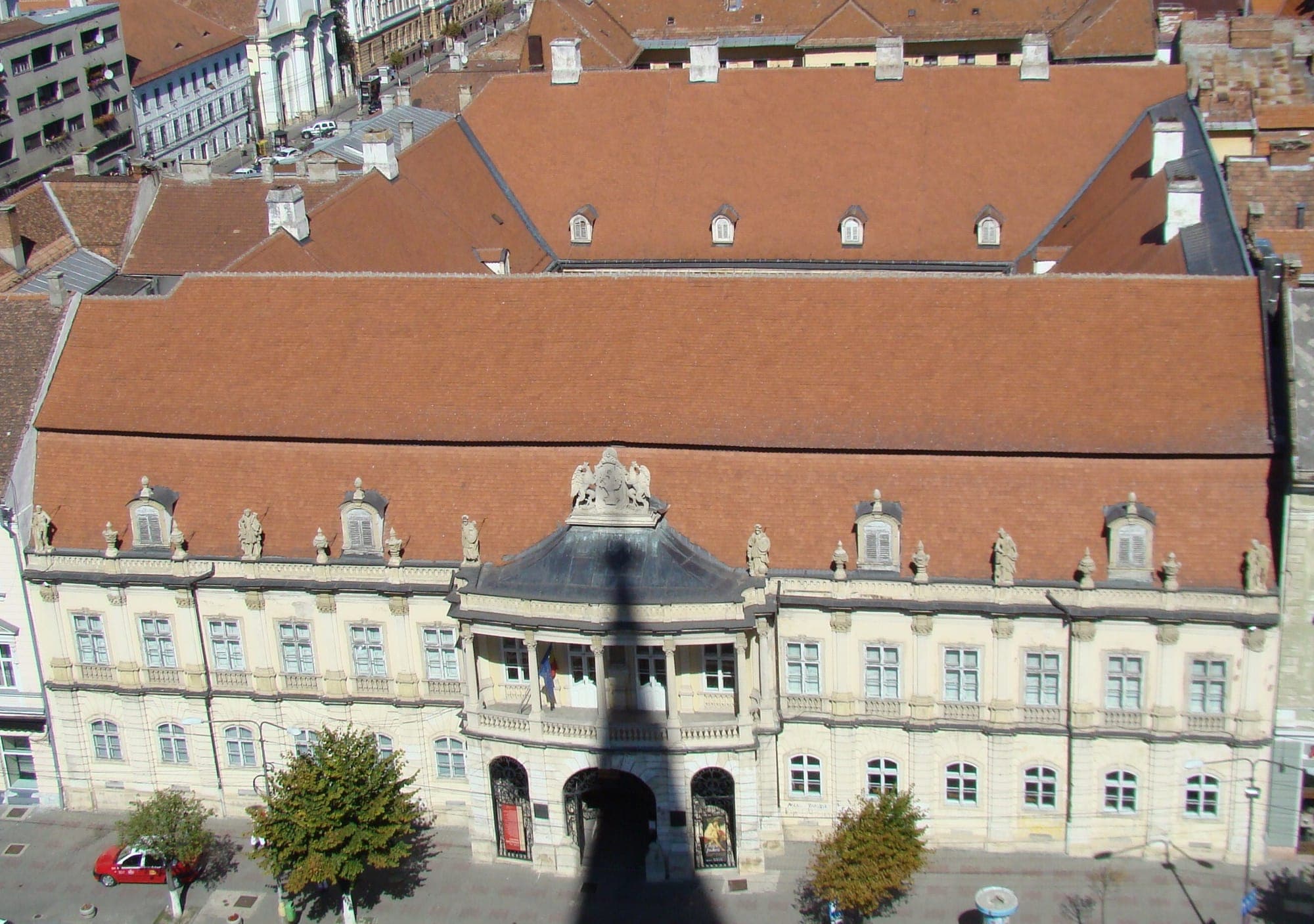 Fațada palatului spre Piața Unirii, văzută de sus, din turnul Bisericii Sfântul Mihail, cu acoperișul de țiglă, statuile de pe cornișă și balconul de deasupra porții