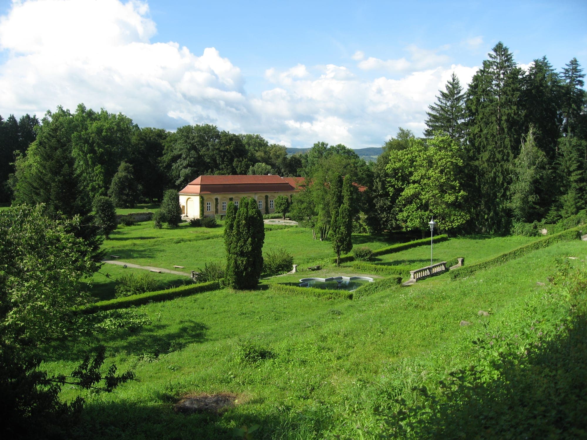 Der barocke Terrassengarten mit dem Becken und der gelben Orangerie zwischen hohen Bäumen, von oben gesehen