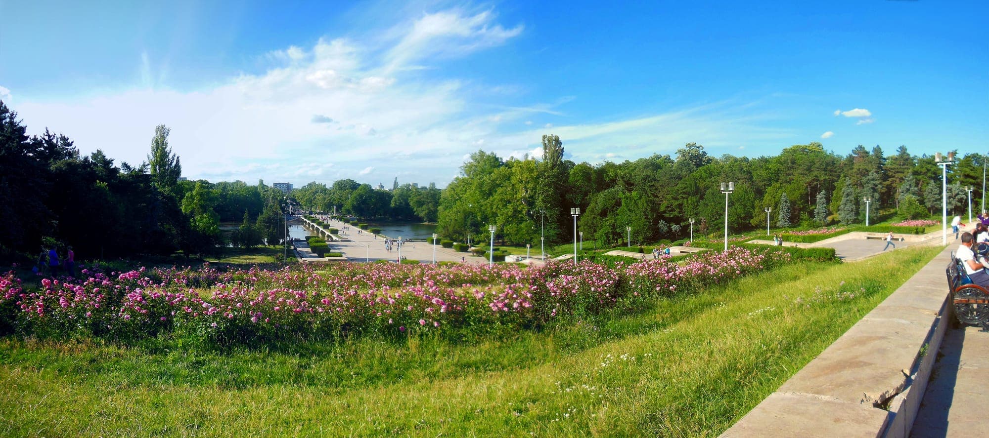 Panorama vom Plateau der Gedenkstätte zum See und zur Zentralallee, mit rosa Rosenbeeten im Vordergrund und grünem Park ringsum