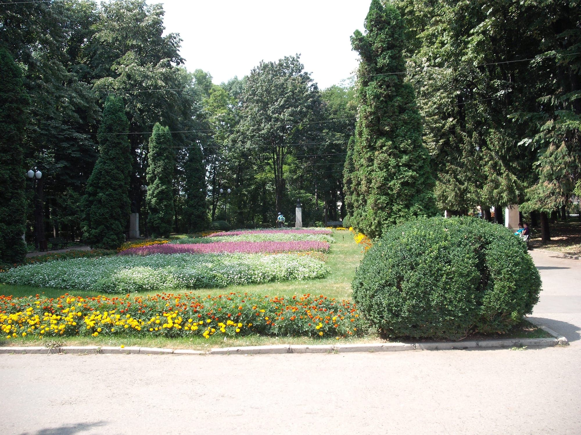 Das sommerliche Blumenparterre auf der Eingangsachse, mit hohen Thujen und alten Bäumen im Hintergrund