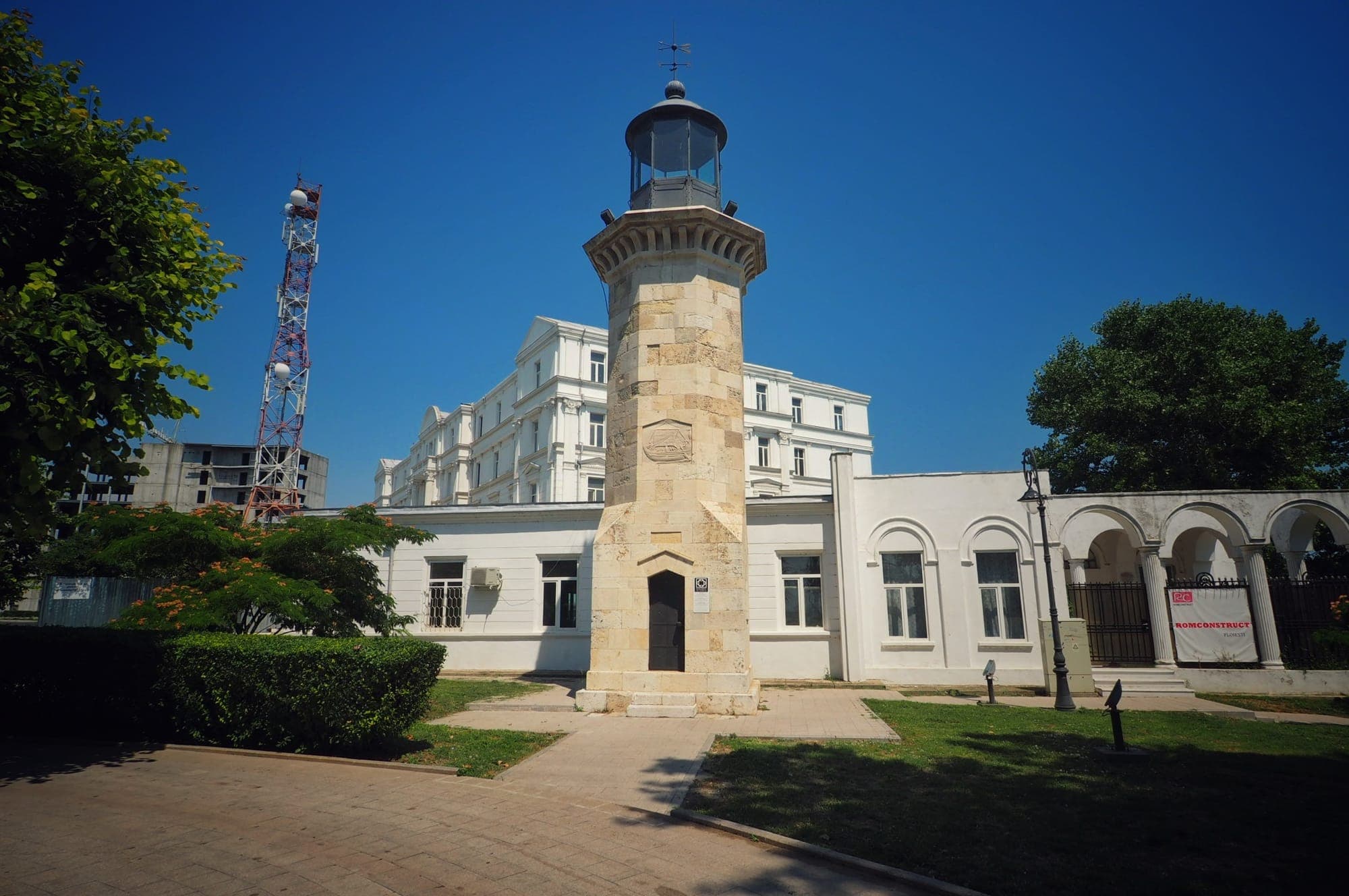 Farul Genovez, un turn octogonal mic din piatră cu lanternă metalică, în fața unor clădiri albe de pe faleză