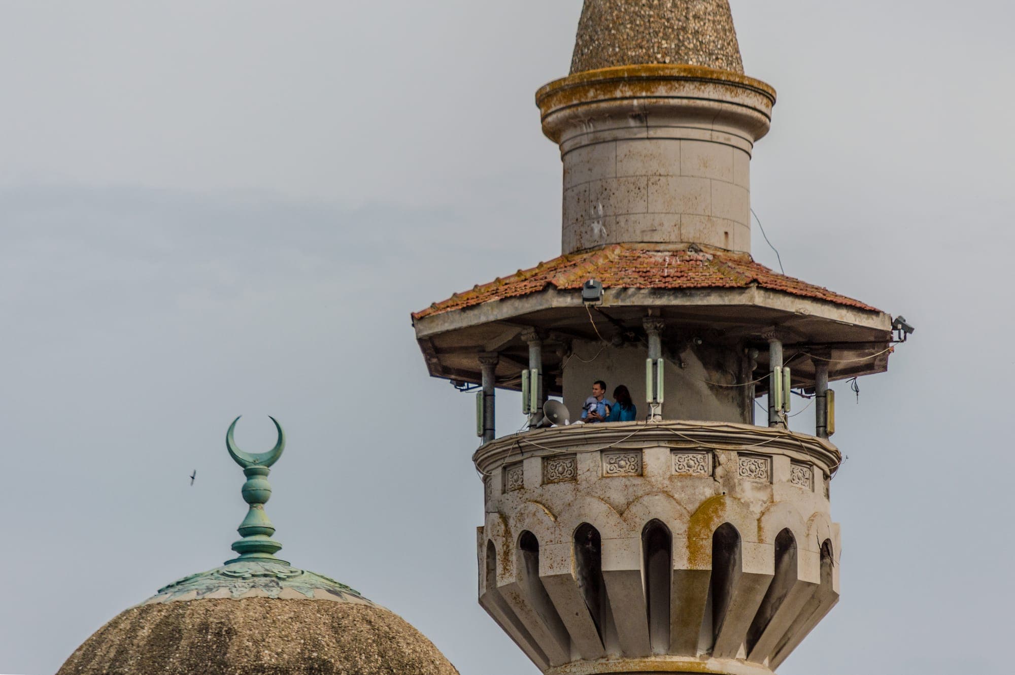 Balconul minaretului Moscheii Carol I, cu doi vizitatori, și semiluna de pe cupolă în prim-plan