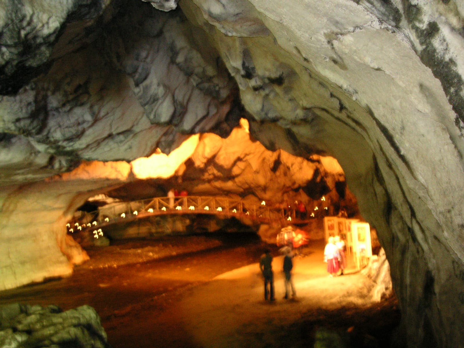 Galeria largă a peșterii, cu o pasarelă de lemn luminată care traversează sala și câțiva vizitatori pe podeaua de pietriș