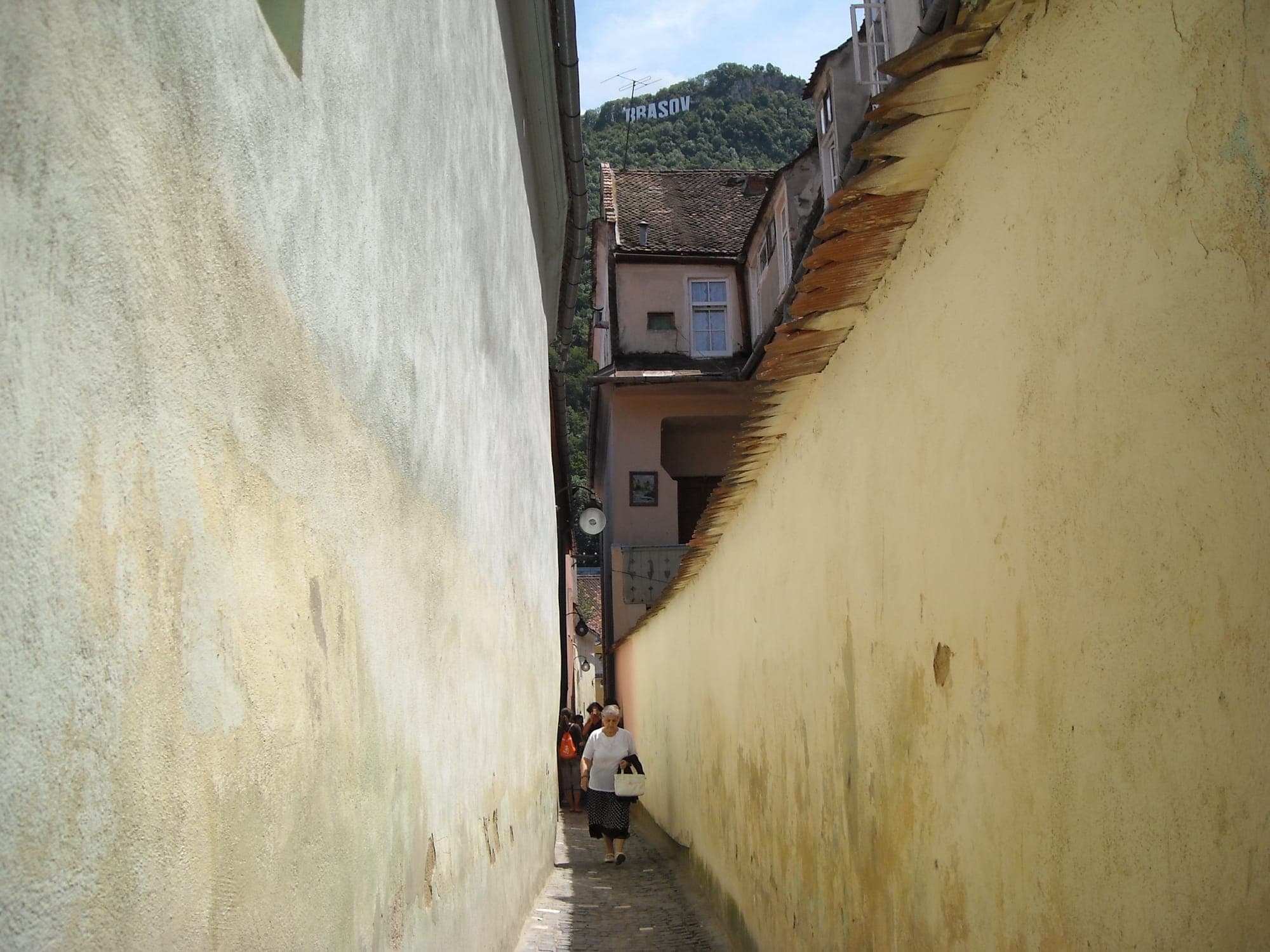 Strada Sforii tra i muri gialli delle case, con una passante in fondo e il Tâmpa con le lettere BRASOV sopra i tetti