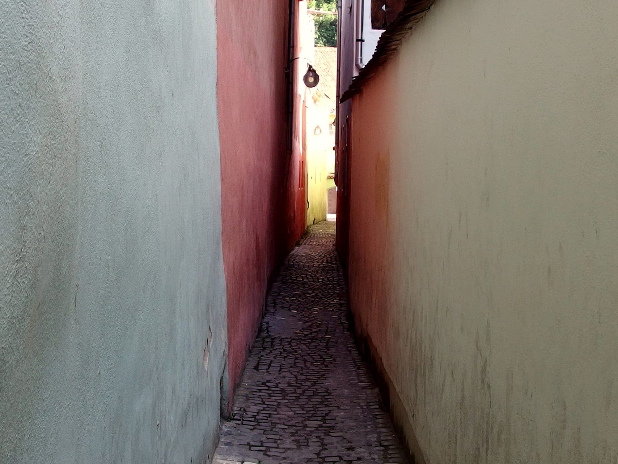 Der mit Pflastersteinen ausgelegte Durchgang zwischen grünen, rosa und gelben Wänden, mit einer Laterne im alten Stil