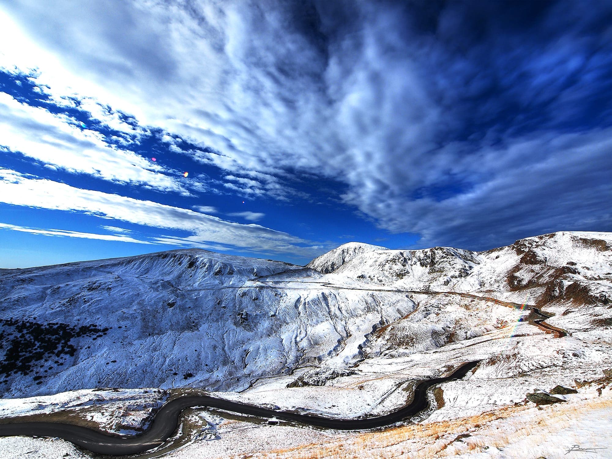 Transalpina șerpuind printre culmi acoperite de prima zăpadă, în octombrie, sub un cer albastru cu nori