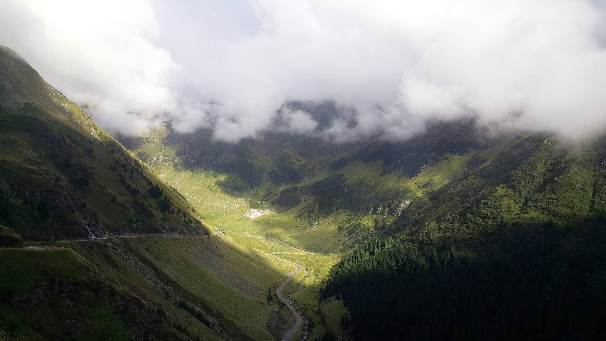 Valea din zona Bâlea, cu drumul pe fundul ei, sub nori joși străpunși de lumina soarelui