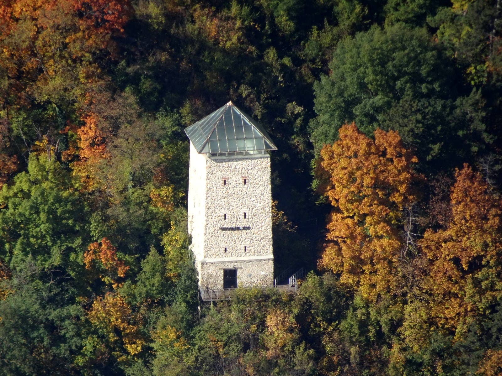La torre bianca di pietra con la piramide di vetro, vista da lontano, in mezzo al bosco autunnale sul versante della collina