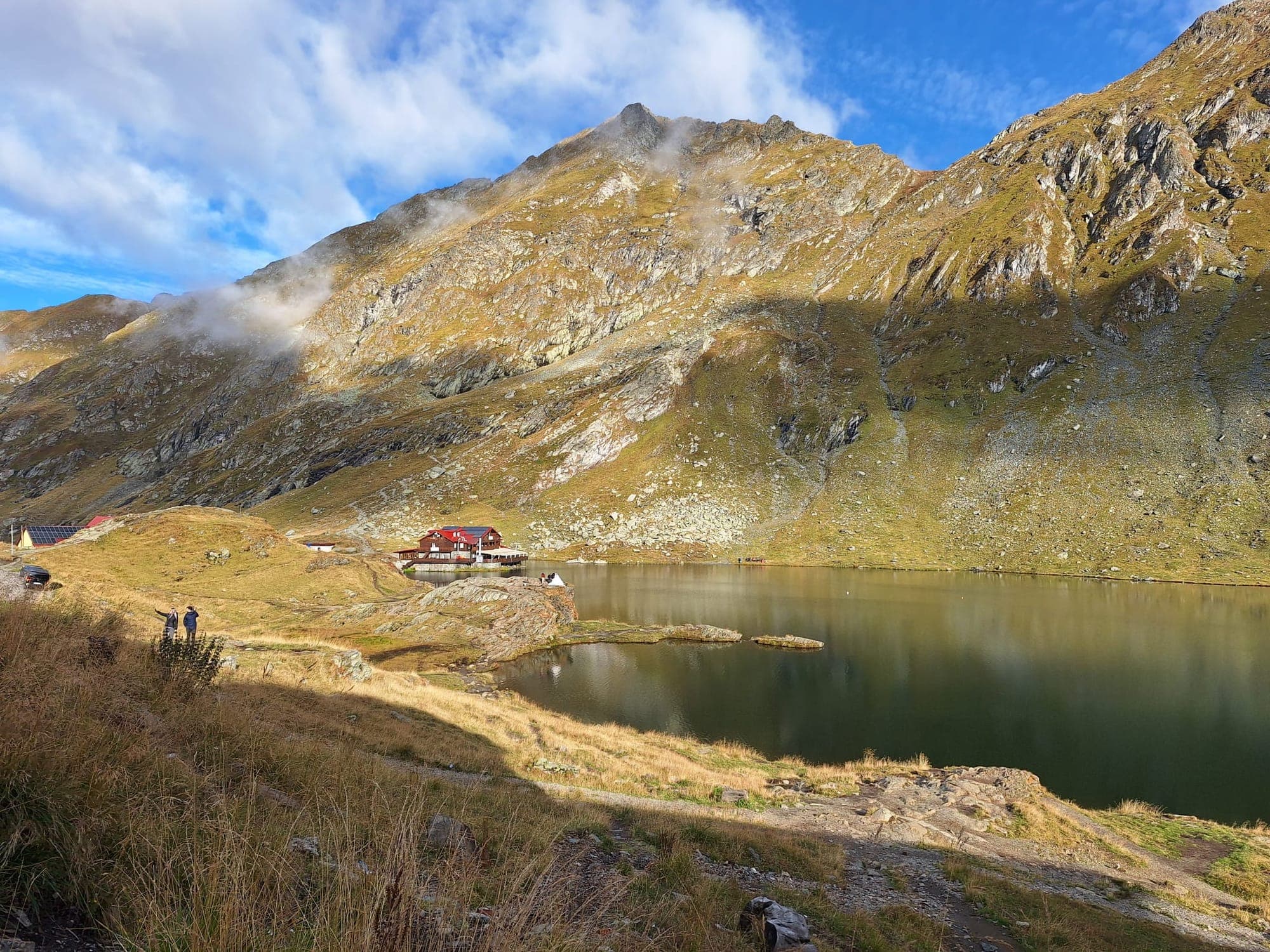 Lacul Bâlea în lumina de toamnă, cu cabana cu acoperiș roșu pe peninsulă și versanții stâncoși ai căldării în spate
