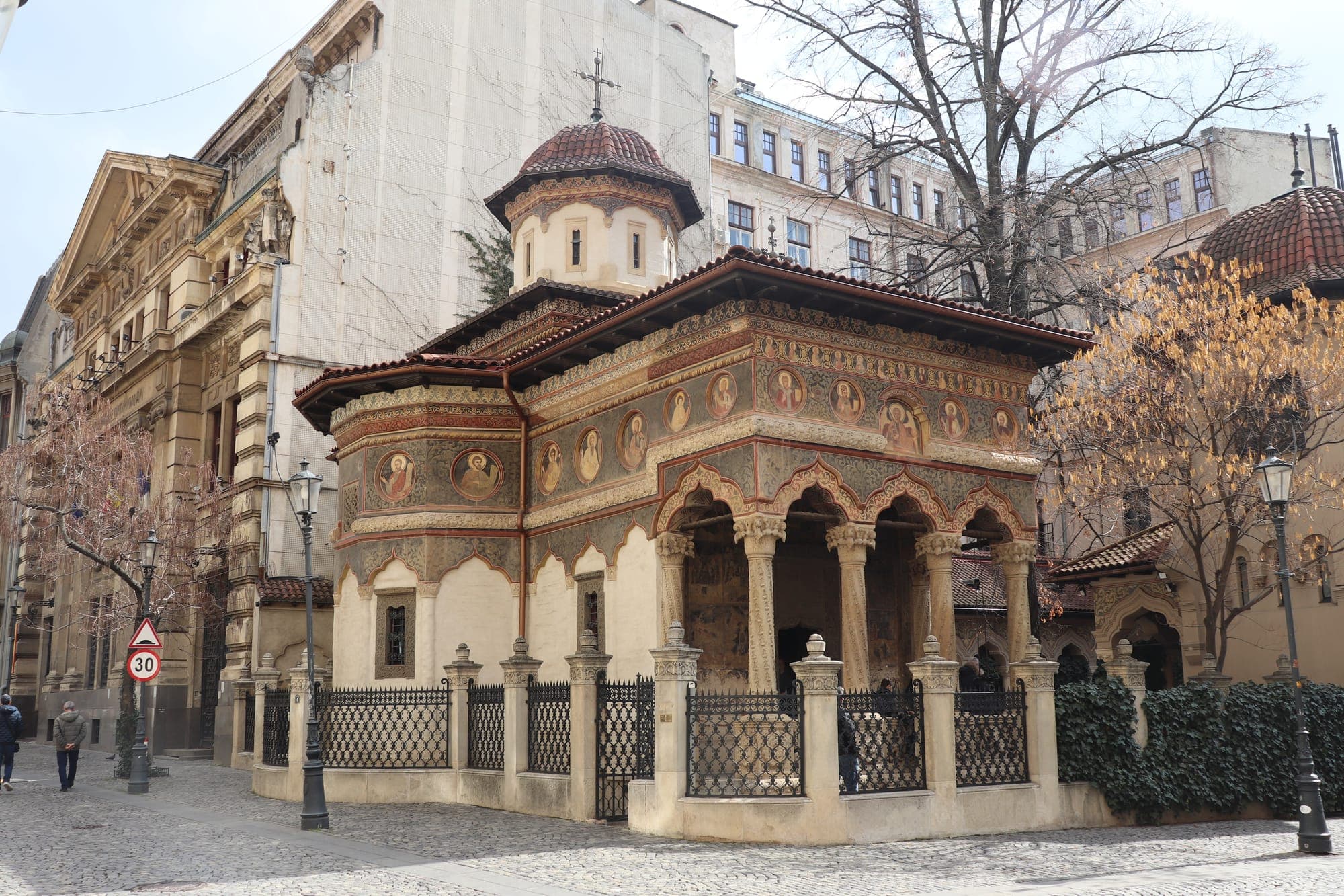 The church porch with carved columns and arches, with painted medallions of saints on the façade and the tower above the tiled roof