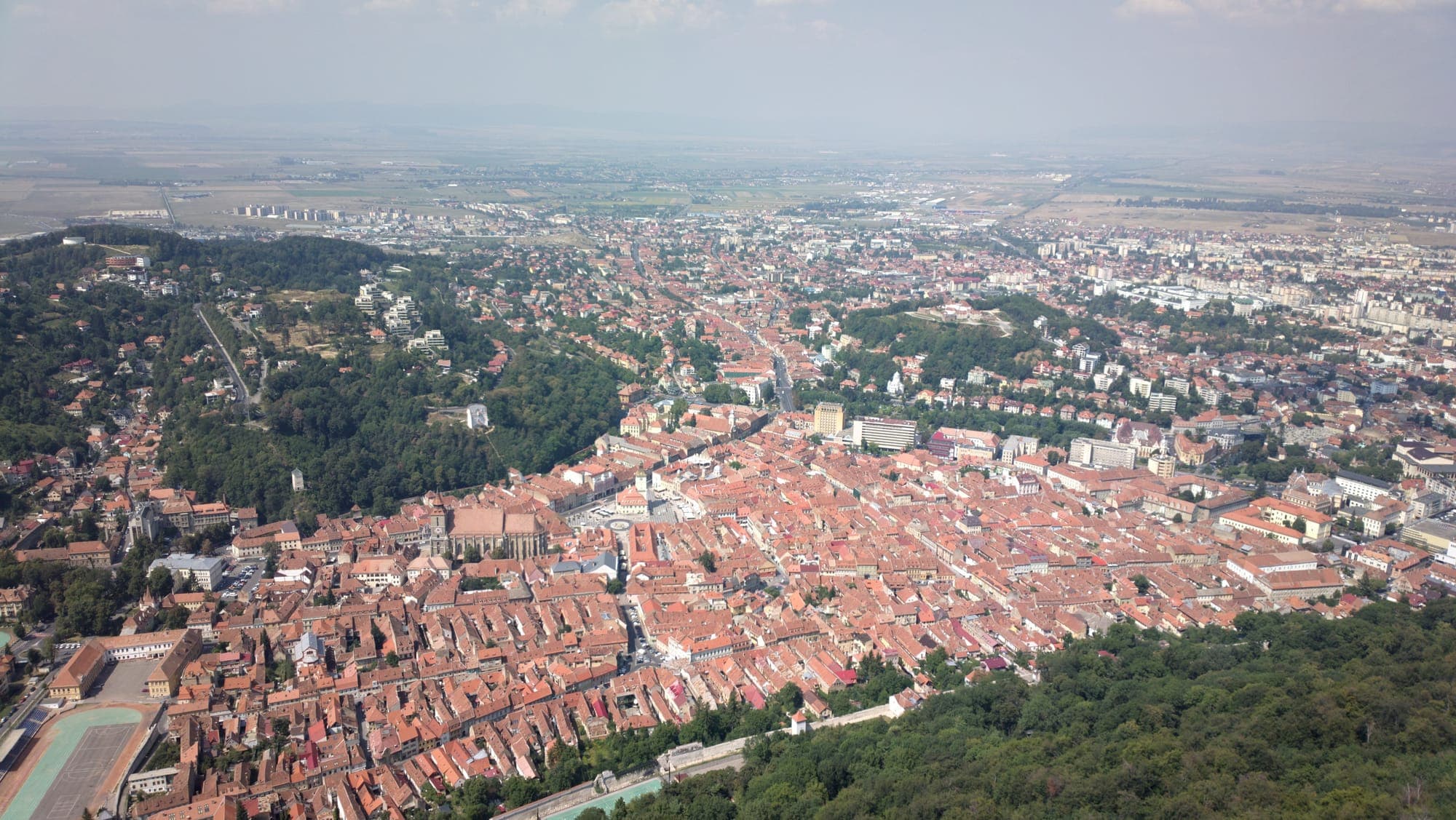 Brașov vista dal Tâmpa: i tetti rossi della città vecchia, la Chiesa Nera e Piața Sfatului, con la città nuova e la pianura in lontananza