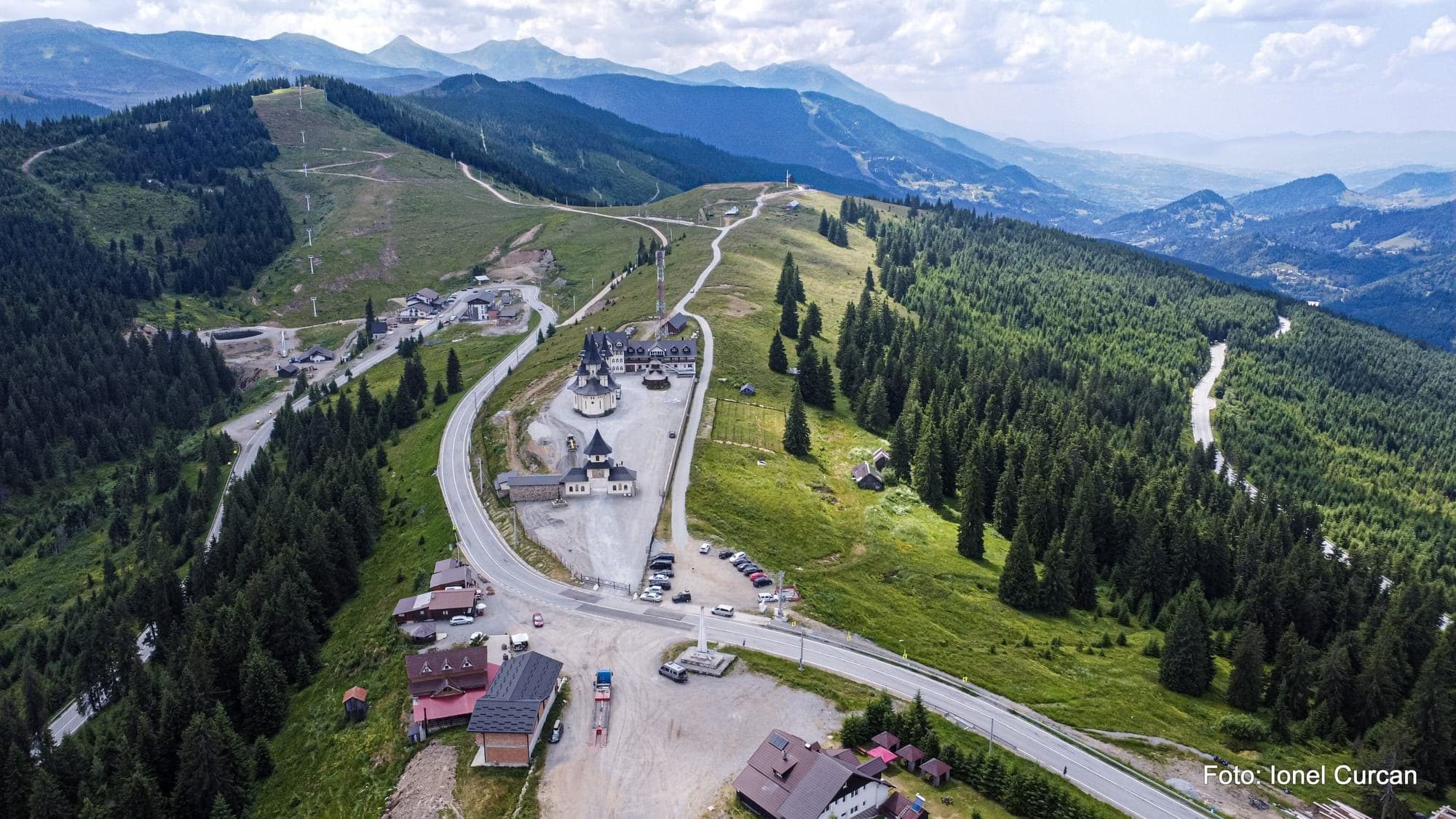 Pasul Prislop văzut de sus: DN18 cotește prin șaua pasului, pe lângă Mănăstirea Prislop și pensiuni, cu vârfurile Munților Rodnei în fundal