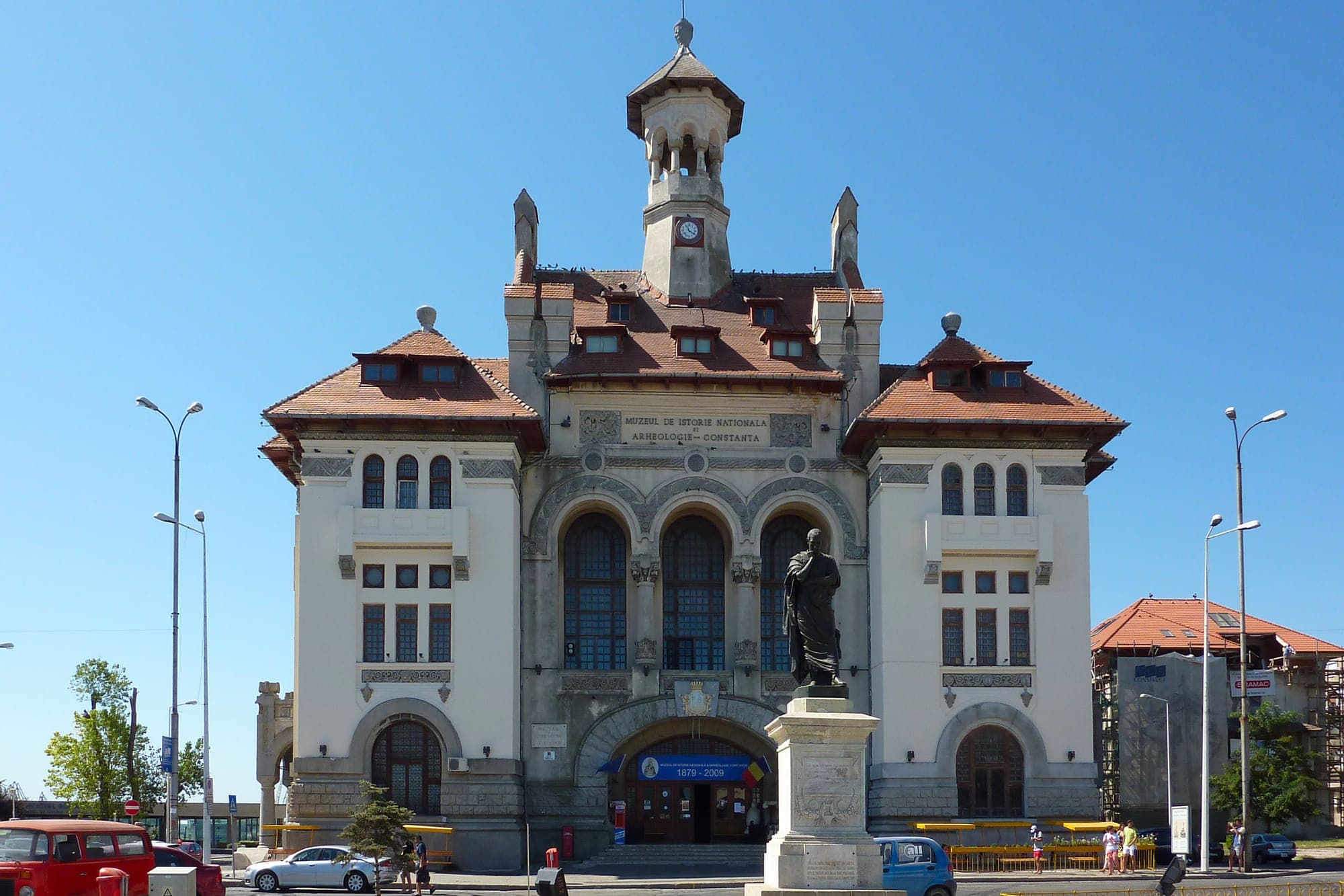 Statuia lui Ovidiu în fața fostei primării neoromânești, cu turn cu ceas și acoperiș de țiglă roșie, azi Muzeul de Istorie
