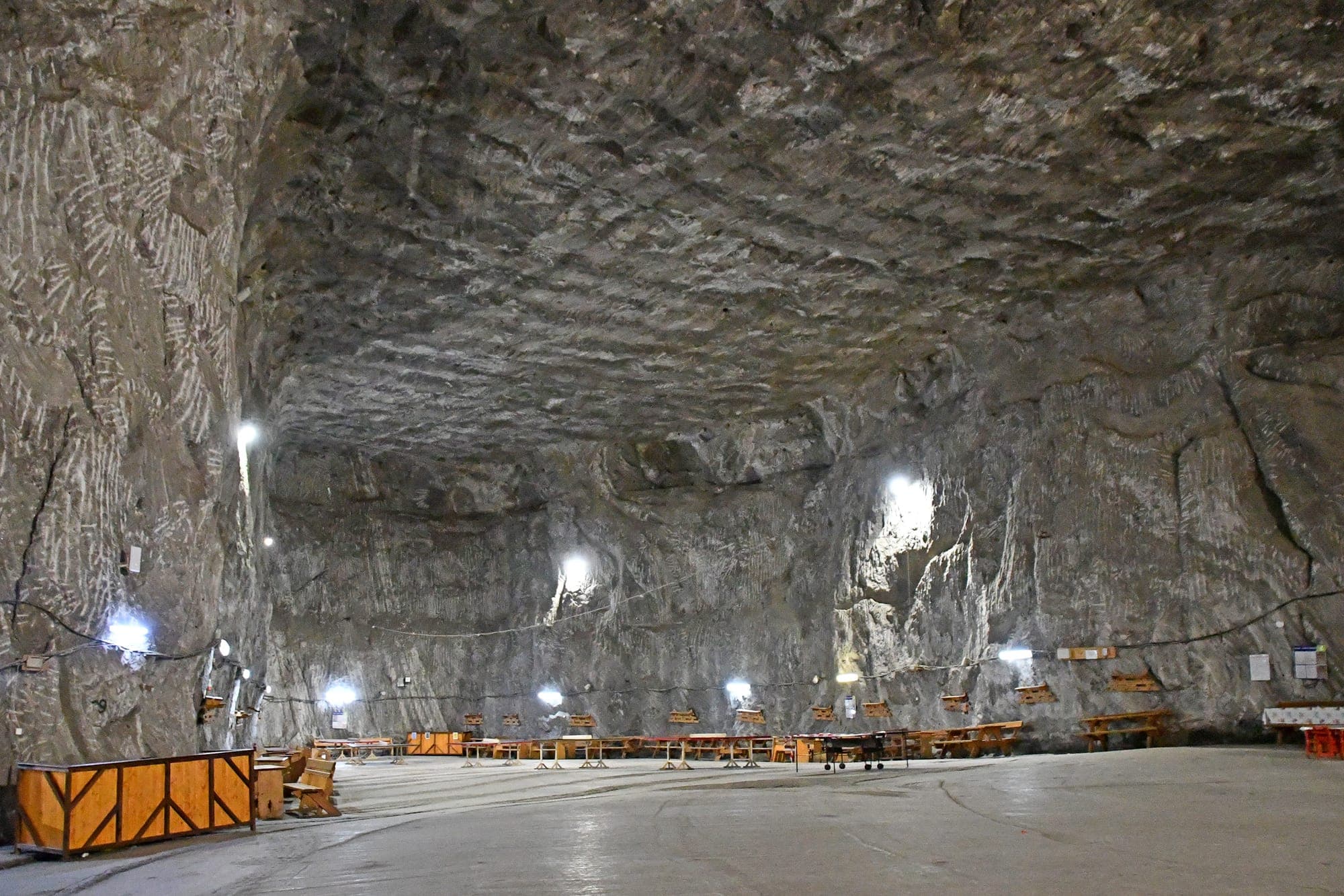 Una dintre sălile de vizitare de la 120 m adâncime, cu tavanul boltit de sare, pereții luminați de lămpi și mese de lemn pe podea, în august 2024